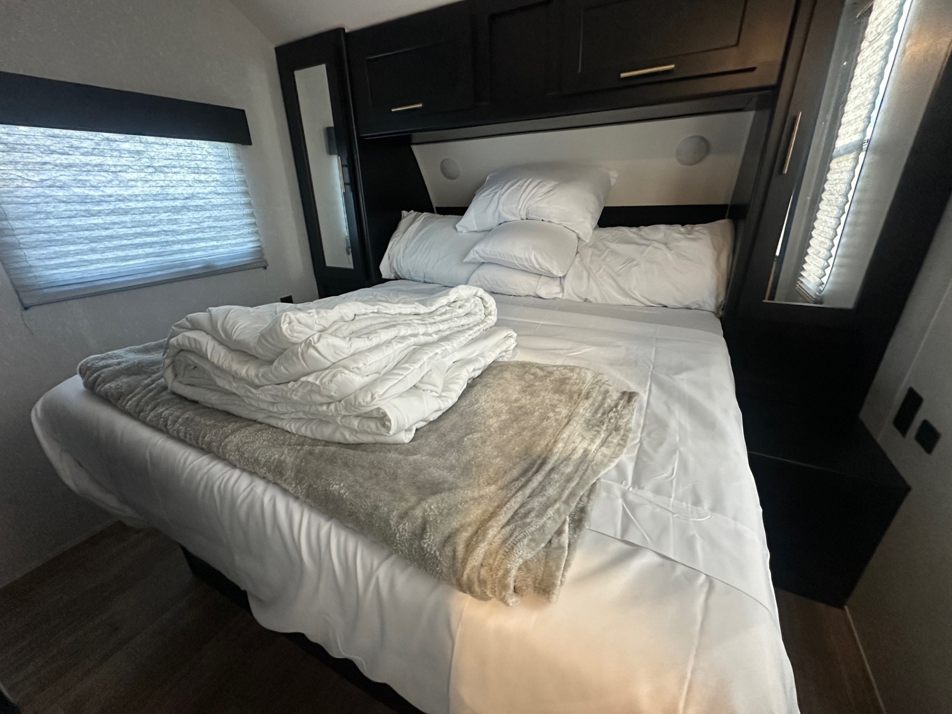 Freshly made bed in an RV rental, with white sheets, pillows, and a cozy blanket. Dark cabinets & window visible.. Forest River Cherokee Grey Wolf 2022