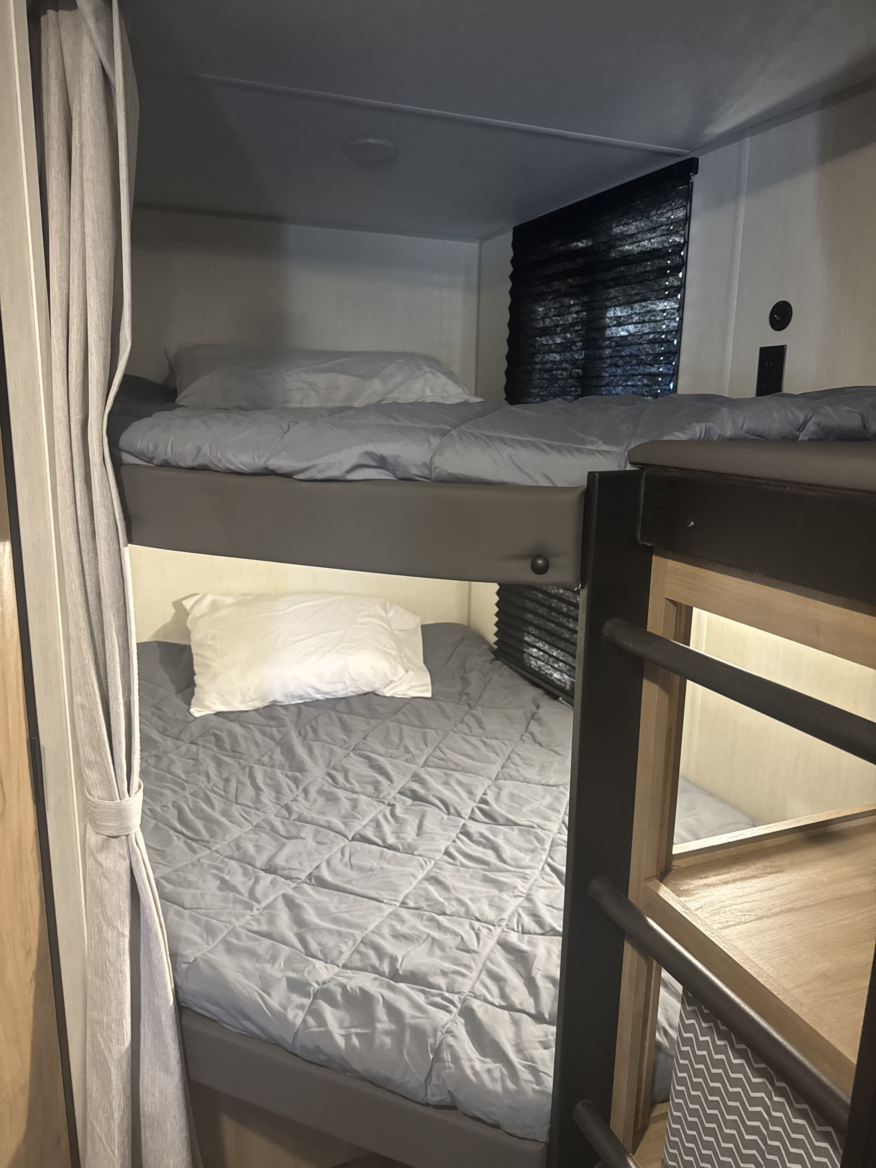 Compact RV rental bunk beds with grey bedding and privacy curtains, perfect for family travel.. Forest River Campsite Reserve 26CJ 2025