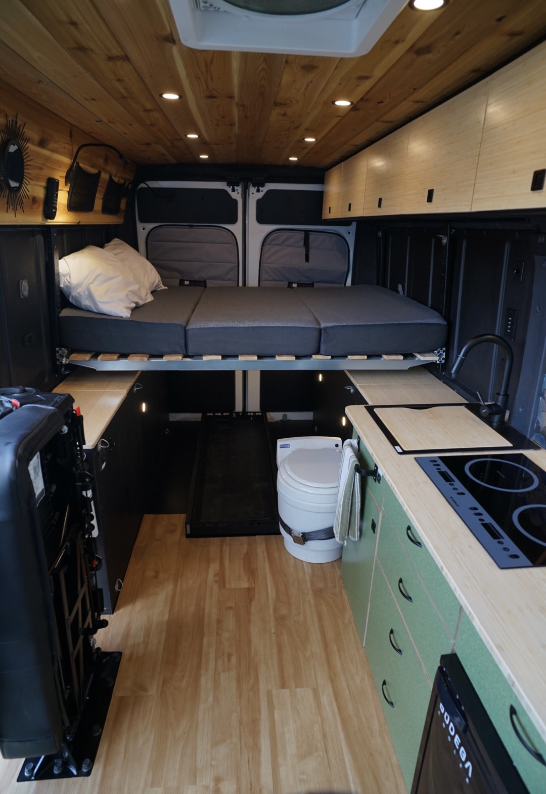 Inside a spacious rv rental camper van: raised bed, sleek kitchen, and toilet. Features wood ceilings and light floors.. Ram Promaster 2023