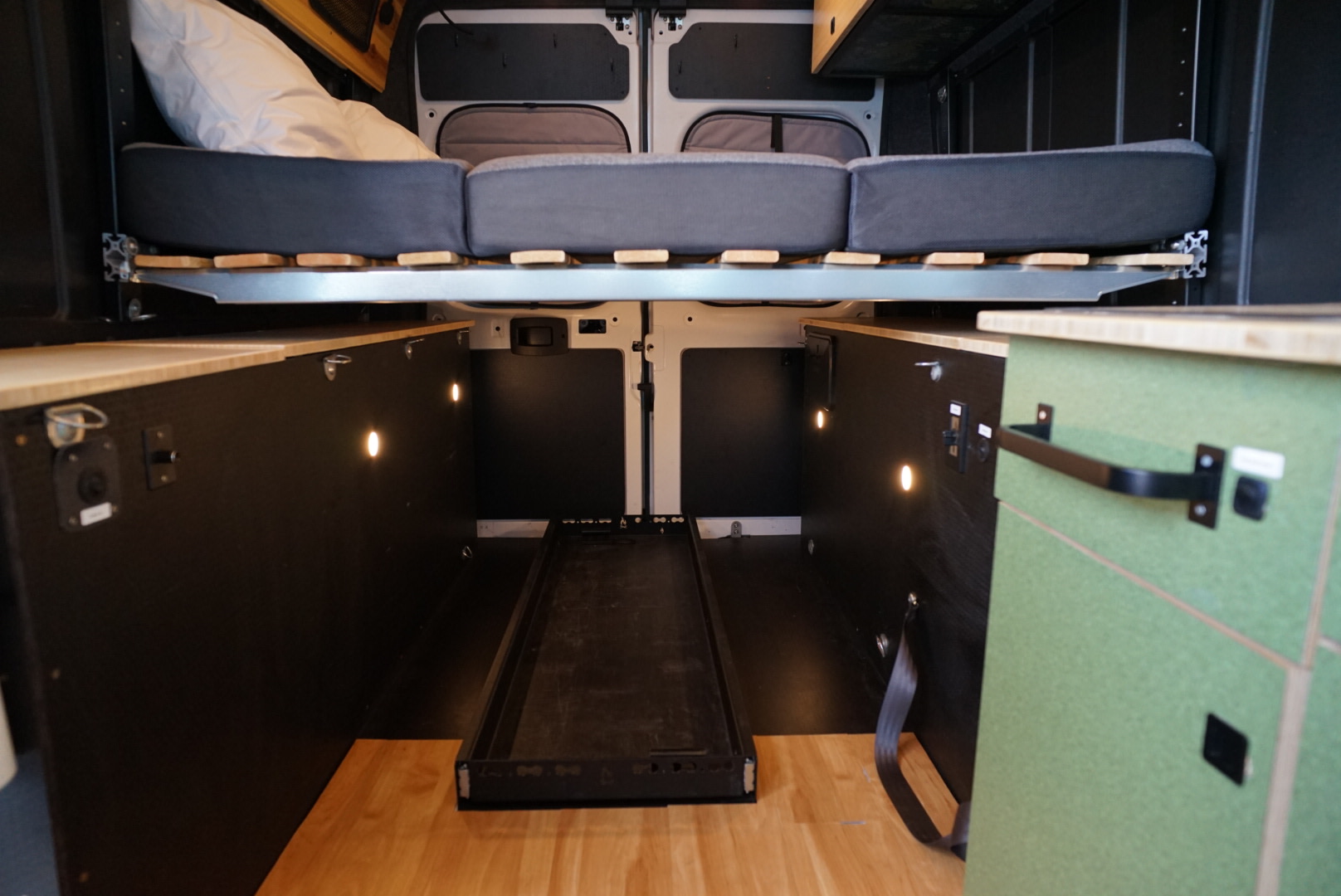 RV rental: Interior of a camper van, showcasing a raised bed, under-bed storage with lighting, and a pull-out tray.. Ram Promaster 2023