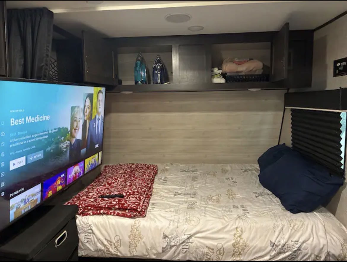 Cozy RV rental bedroom featuring a bed, large TV showing "Best Medicine," and overhead storage cabinets.. Jayco Jay Flight SLX 2023