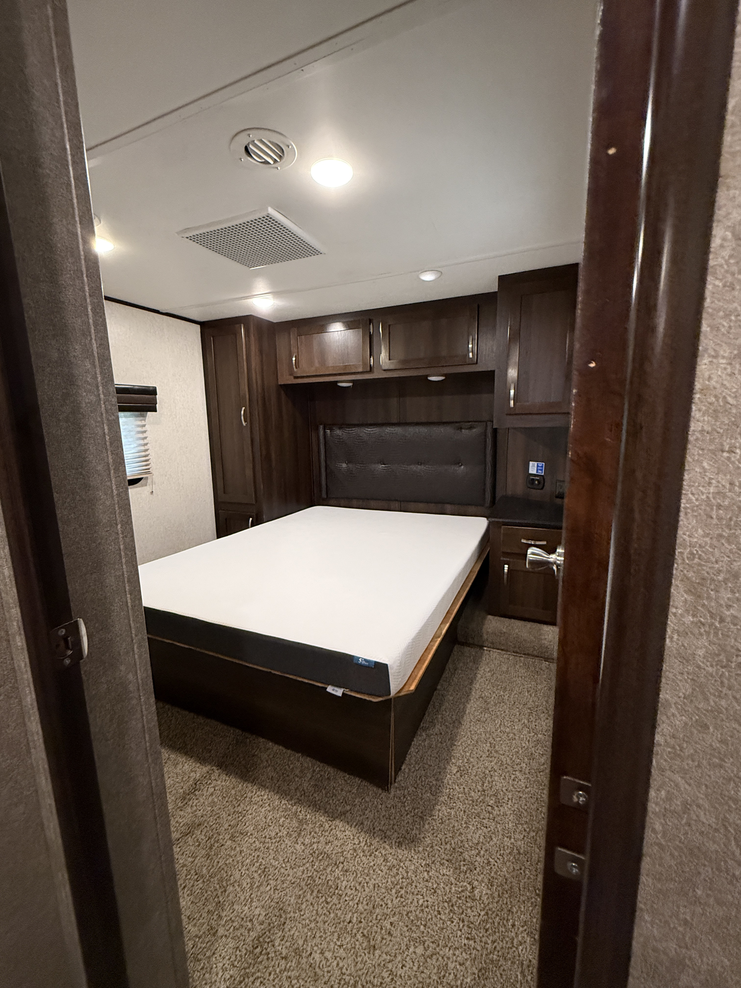 This RV rental bedroom features a comfortable bed, dark wood storage cabinets, ceiling lights, and an air vent, ideal for mobile living.. Jayco Talon 413TJ18B 2018