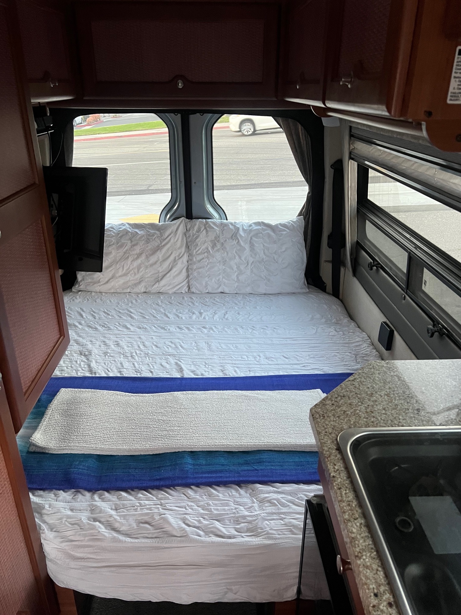 Cozy RV rental interior featuring a neatly made bed, mounted TV, and compact kitchen counter with a stove. Ideal for travel.. Roadtrek Roadtrek Class B 2008