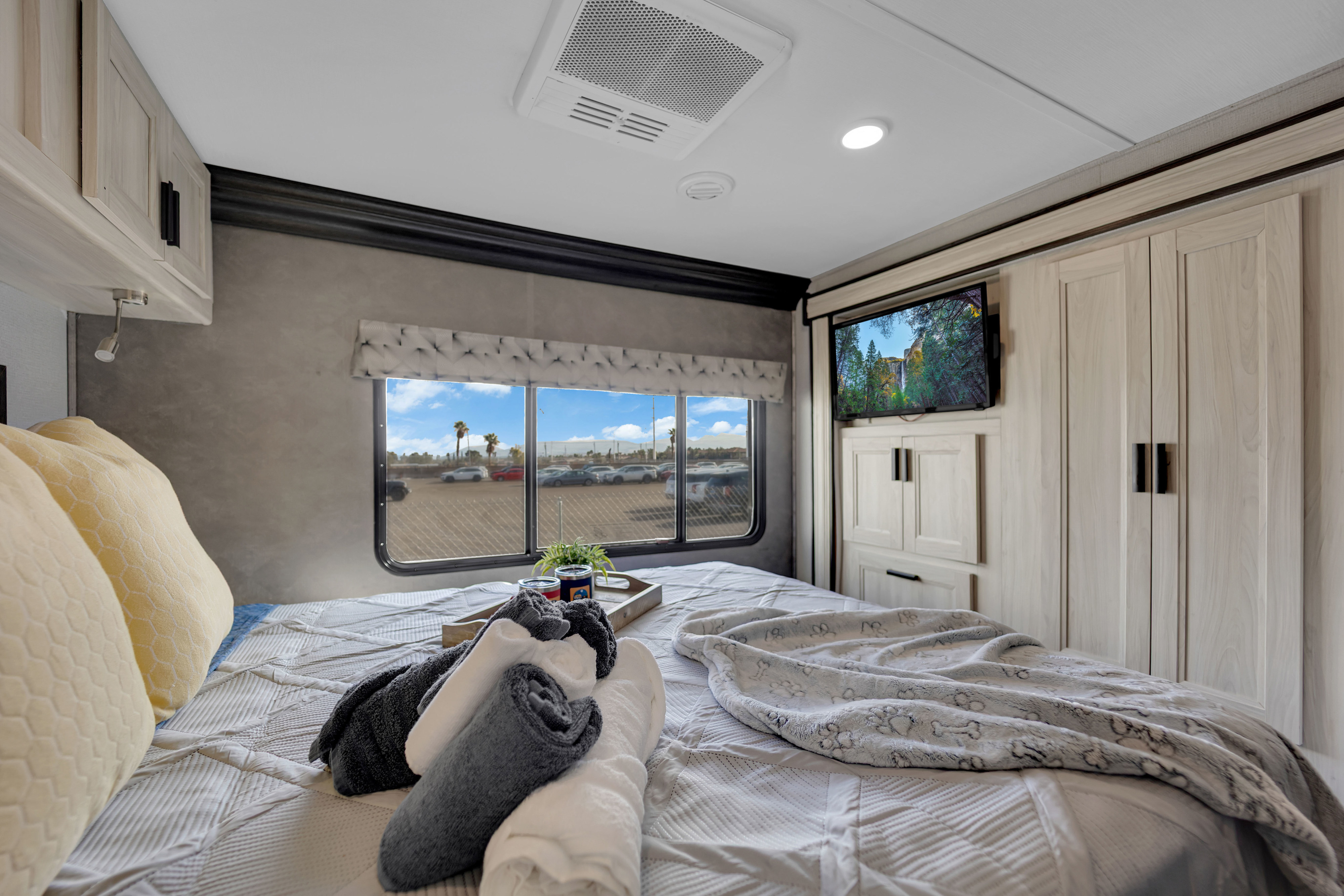 Cozy RV rental bedroom featuring a comfortable bed, TV, light cabinets, and a window view of a parking lot.. Forest River Sunseeker 2021