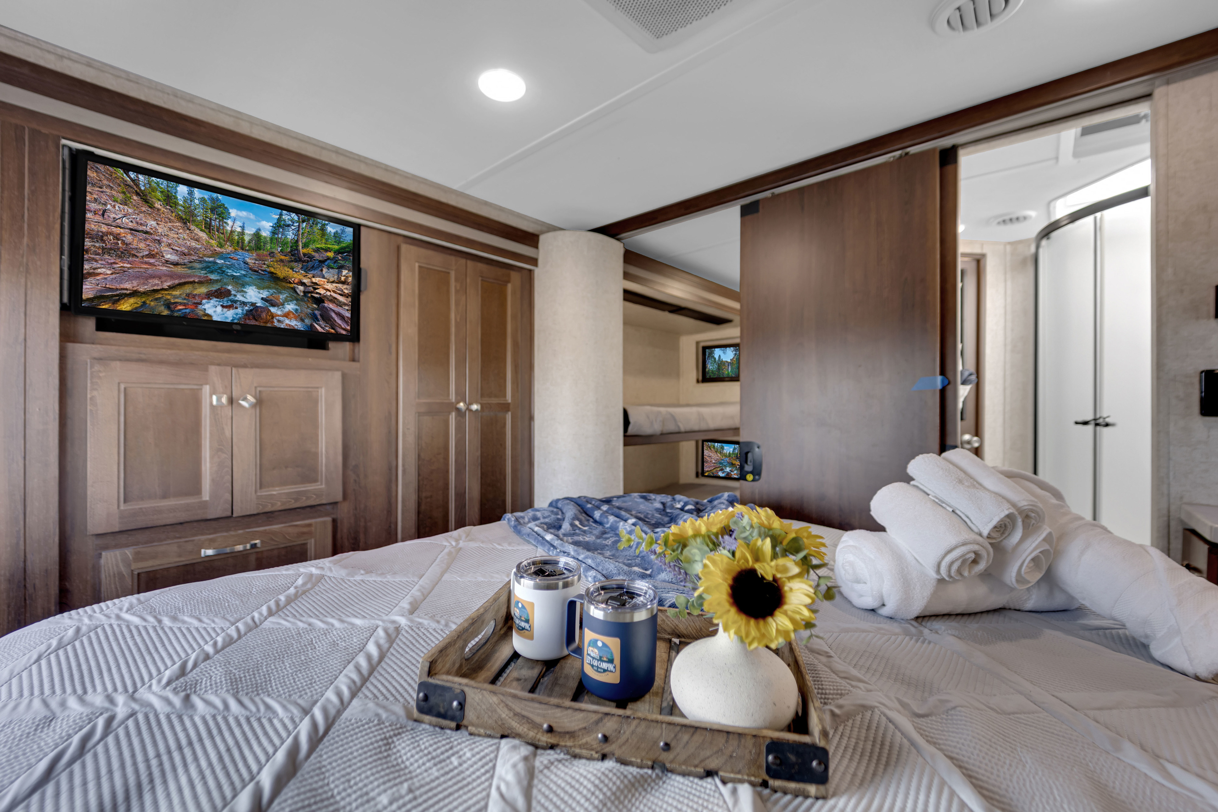 RV rental master suite with a comfy bed, TV, wood cabinets, and access to a bunk area and bathroom. Breakfast tray with flowers.. Forest River Forester 2020