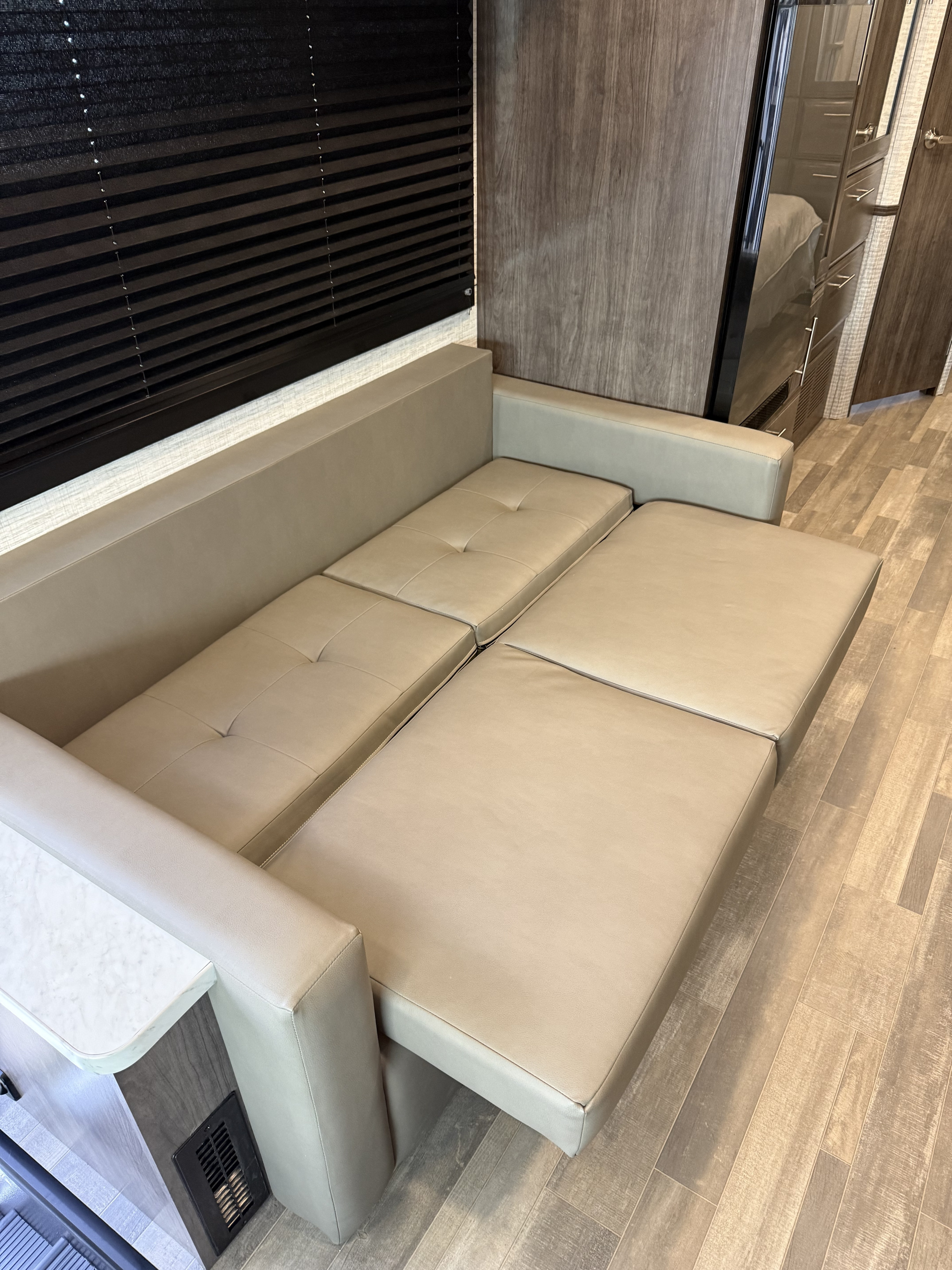RV rental: Light beige sofa bed extended in a modern camper interior with wood-look flooring and dark window blinds.. Entegra Coach Vision SE 2025