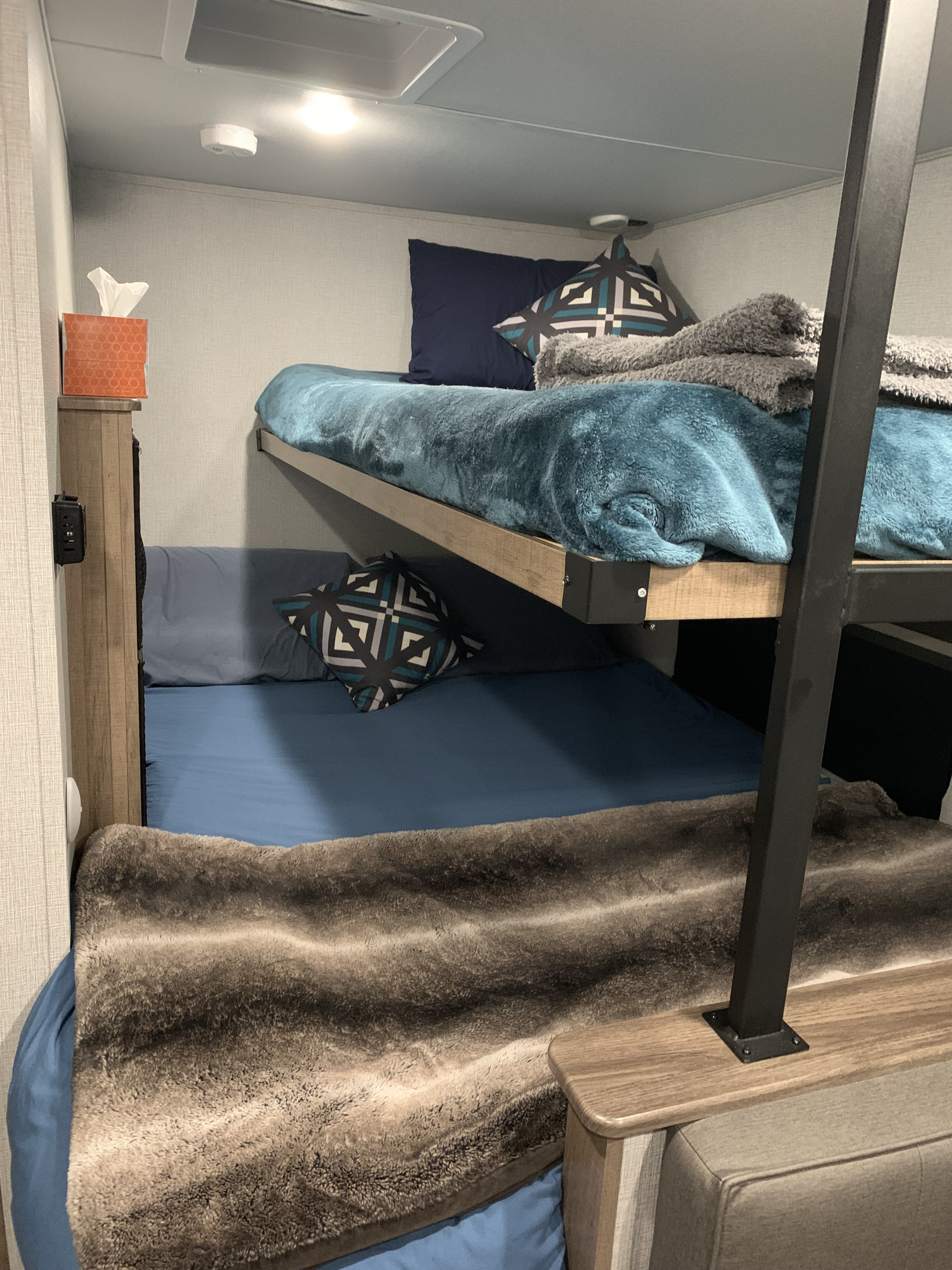 Cozy bunk beds in an RV rental interior. The upper bunk has blue bedding, the lower has a fuzzy blanket; perfect for families.. Grand Design Imagine AIM 2023