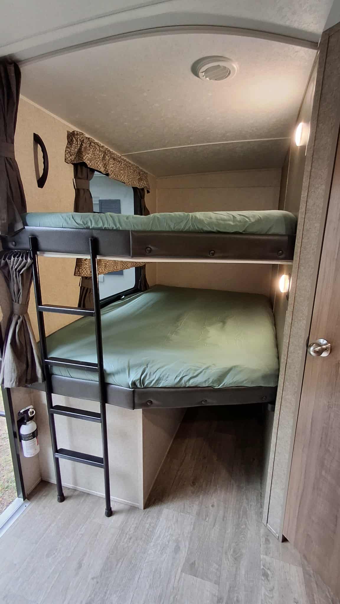 Spacious rv rental bunk beds with a ladder, green linens, and a wall-mounted fire extinguisher for guest safety.. Forest River Rockwood Ultra Lite 2019