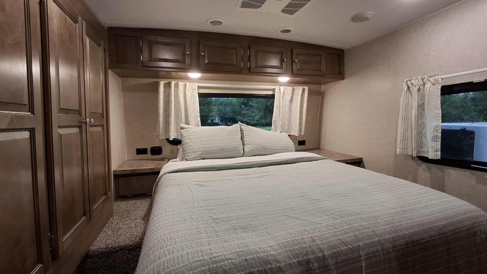 RV rental bedroom interior featuring a comfortable bed, window with curtains, and overhead storage cabinets.. Forest River Rockwood Ultra Lite 2019
