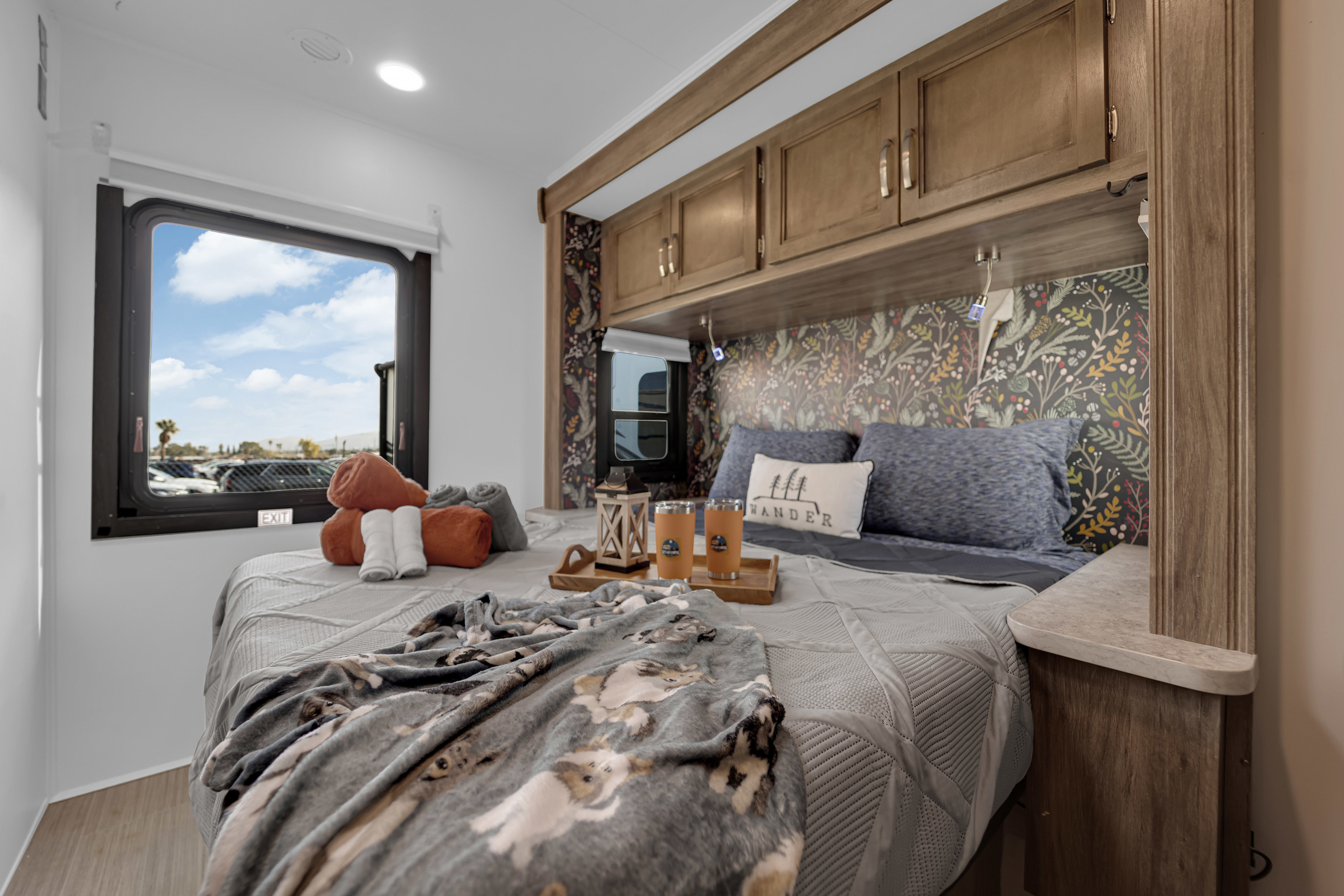 Experience comfort in this RV rental bedroom. Features a cozy bed, patterned wall, storage cabinets, and a window overlooking a parking area.. Jayco Redhawk 2021