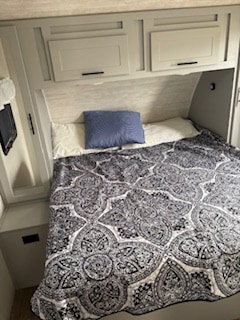 This RV rental offers a cozy bedroom with a patterned quilt, blue pillow, and overhead storage. Ideal for your travel comfort.. Forest River Vibe 2024