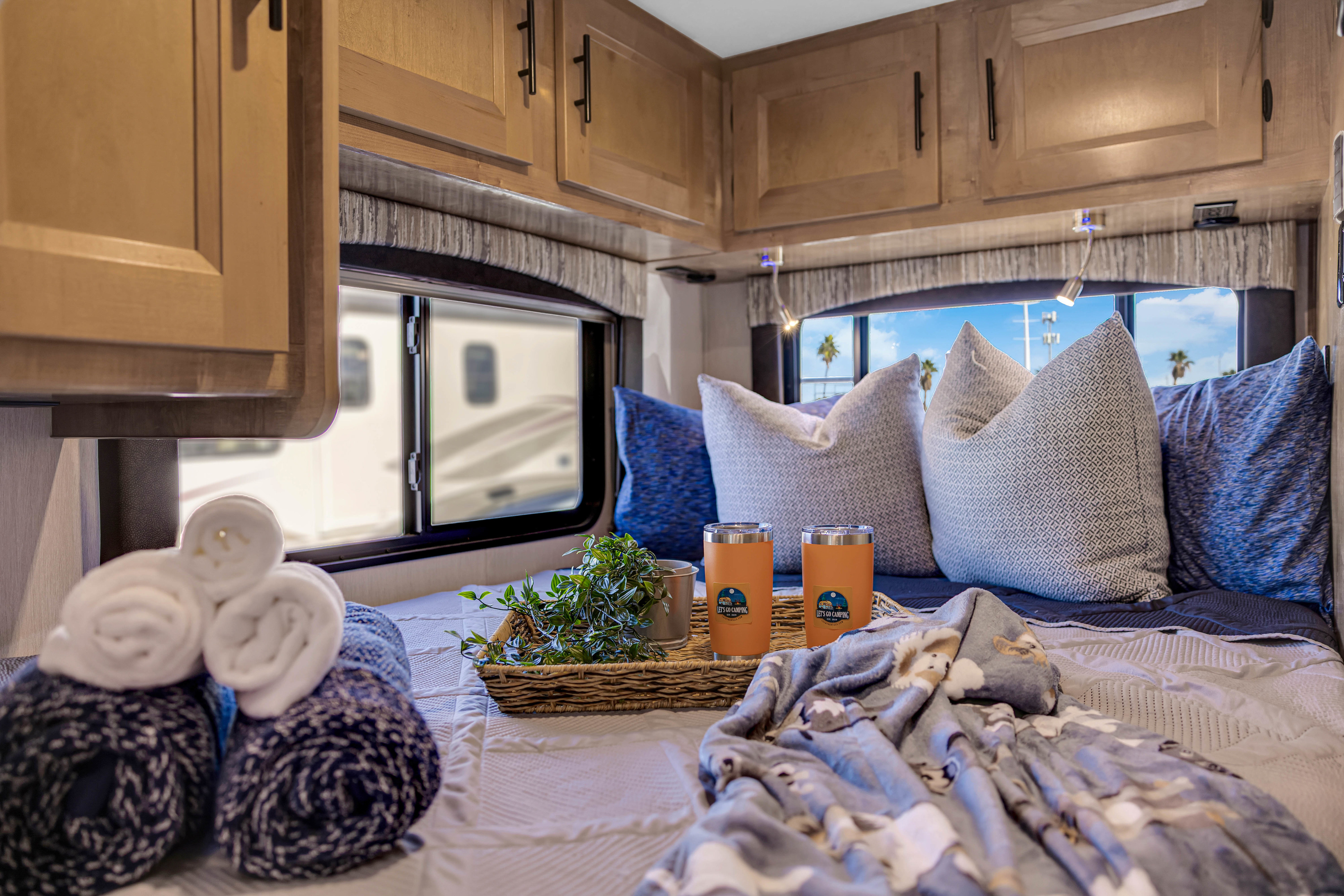 Cozy RV rental bedroom featuring comfortable bedding, custom tumblers, and a serene view of palm trees for your camping trip.. Coachmen Leprechaun 2021