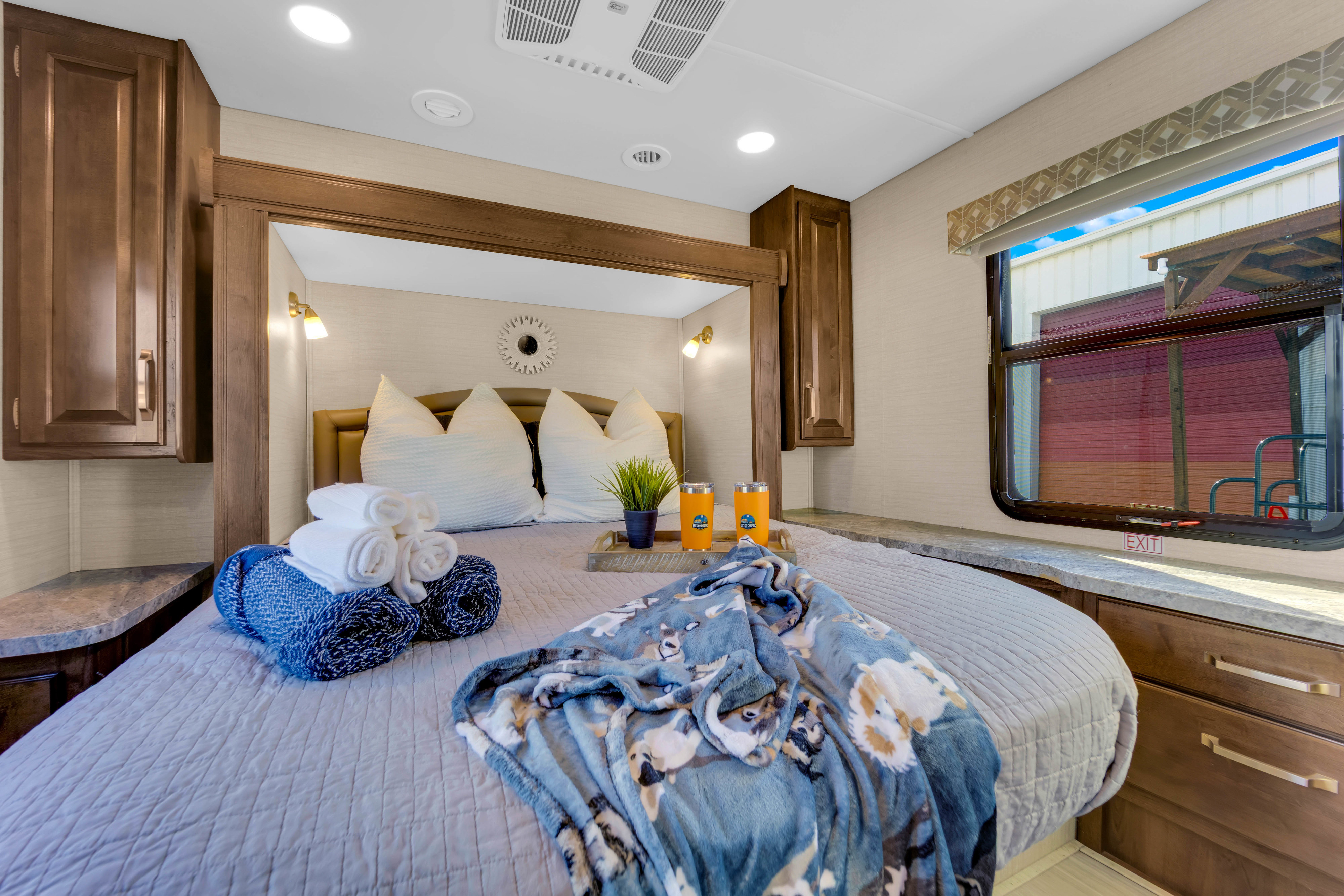 Cozy RV rental bedroom with a comfortable bed, dog-themed blanket, and essential amenities for your journey.. Jayco Greyhawk 2018
