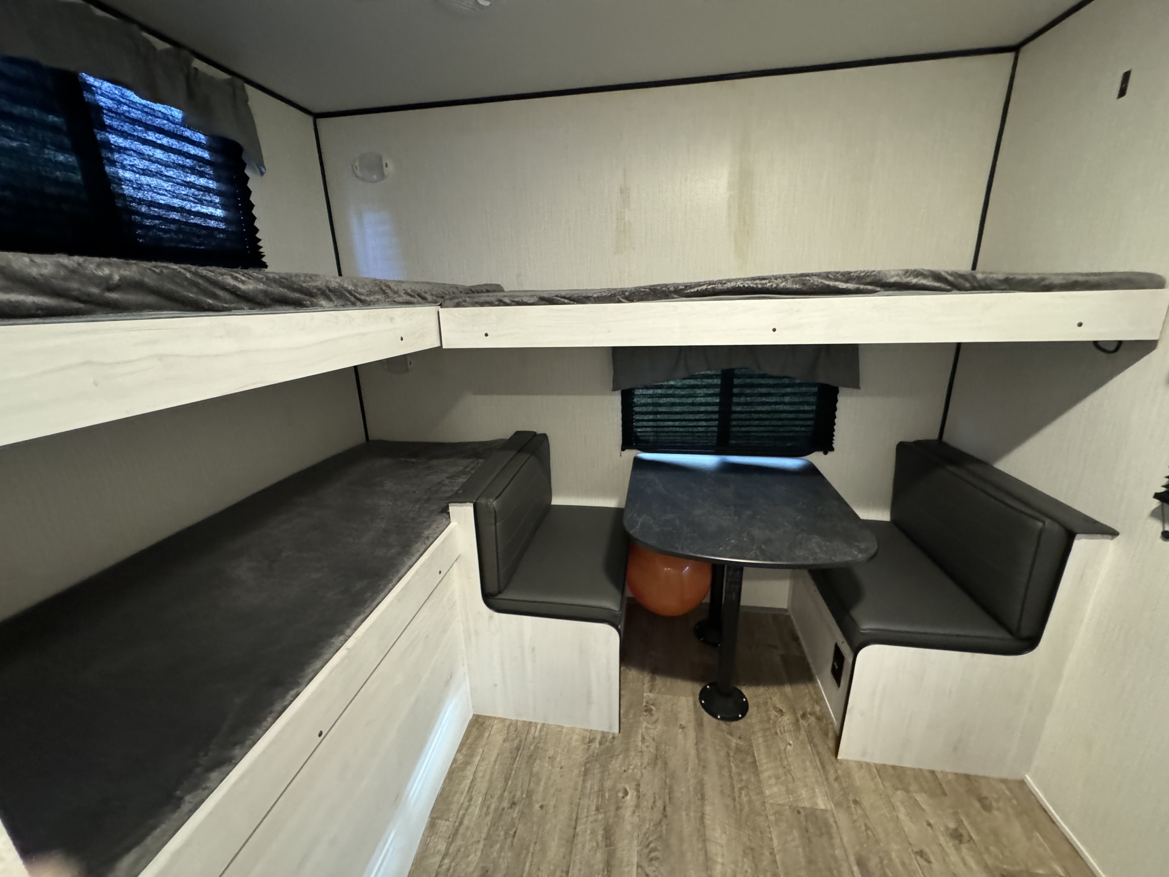This RV rental's interior shows a compact living space with double bunk beds on the left and a dinette on the right, featuring light walls and wood-look flooring.. Heartland RVs Trail Runner 2024