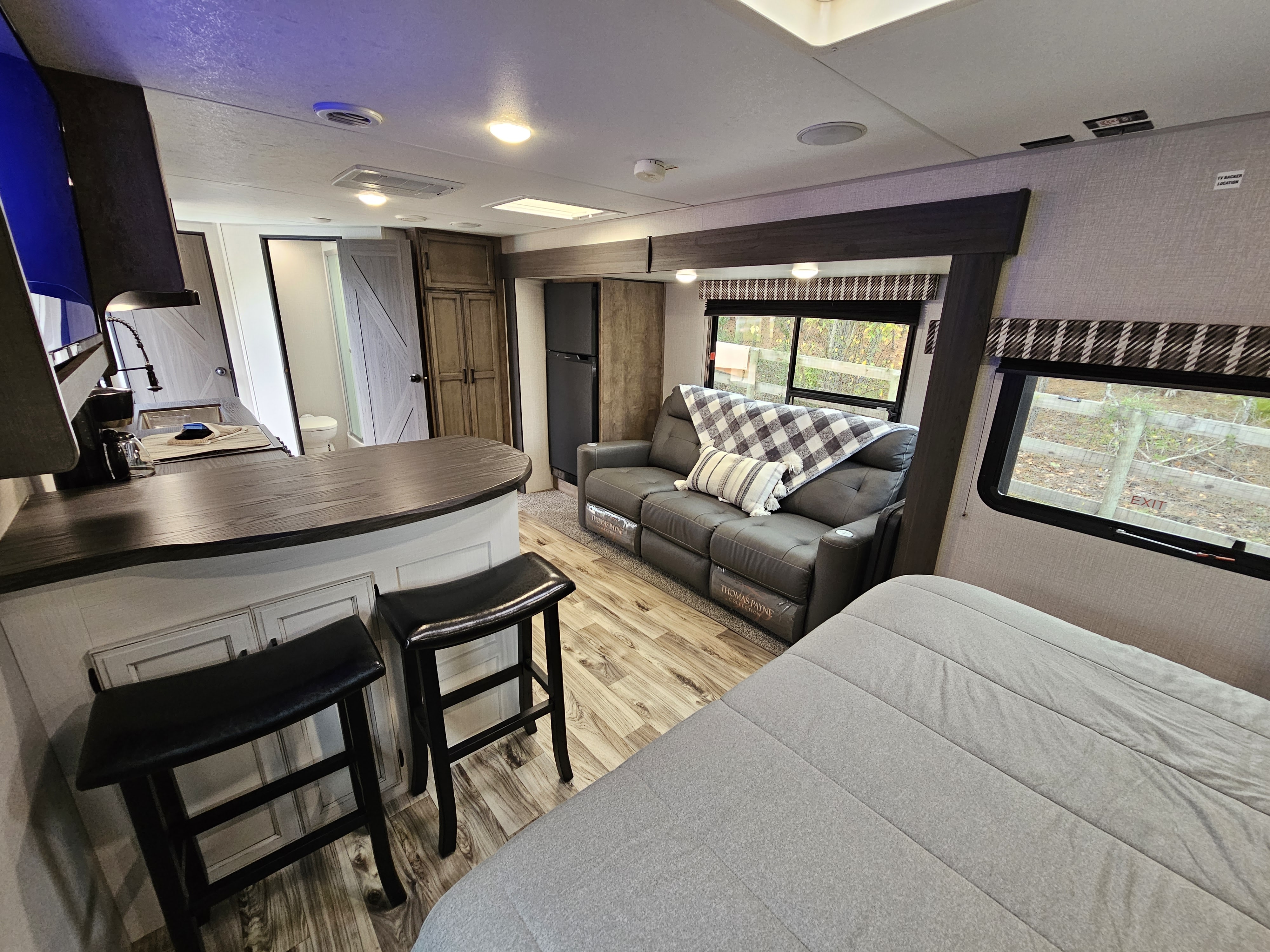 Experience comfort in this modern RV rental. Features include a kitchen counter with stools, a comfy sofa, and a spacious bed.. Venture Stratus 2021