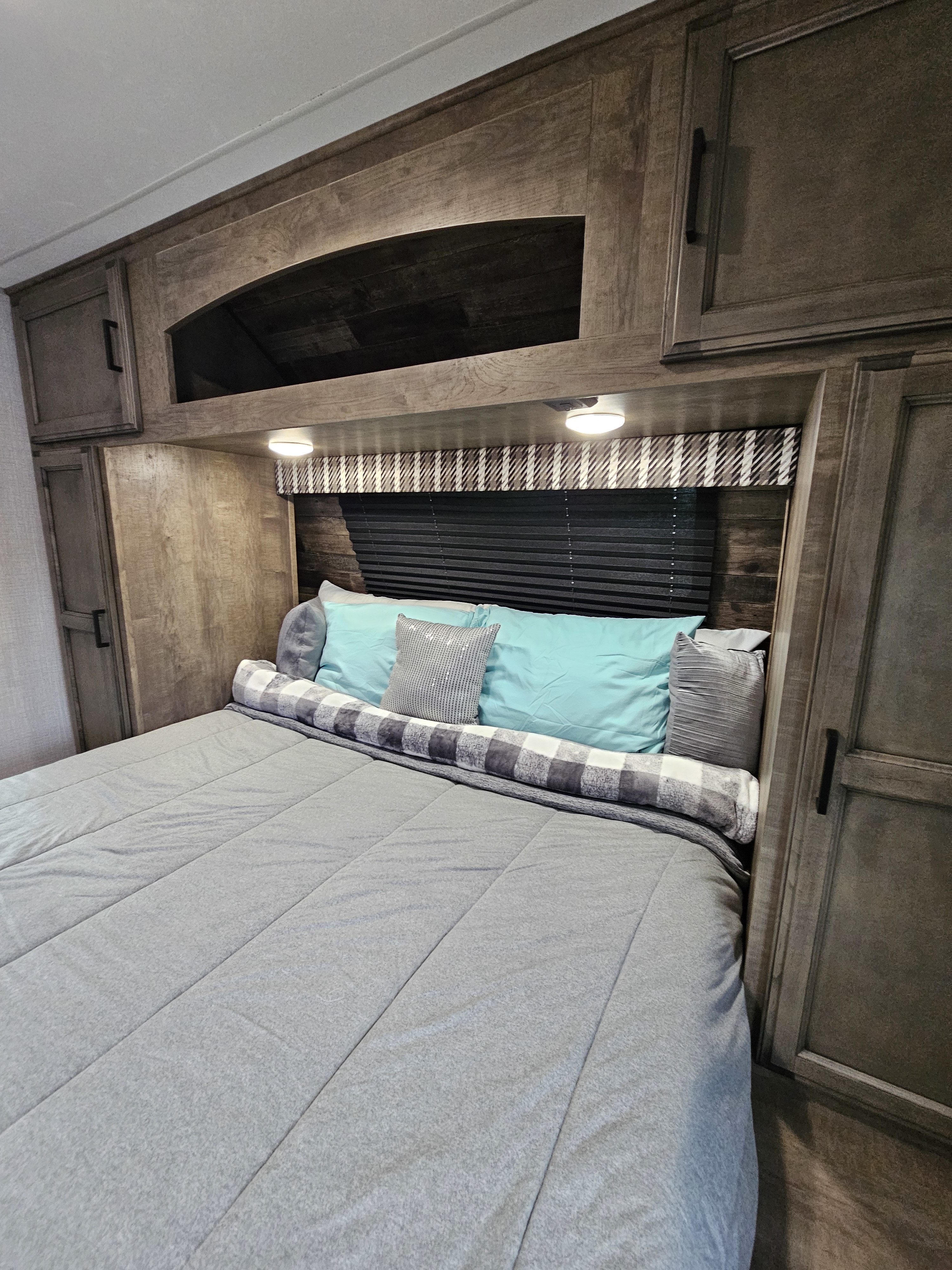 Cozy RV rental bedroom featuring a grey bed, turquoise pillows, built-in wooden cabinets, and overhead lighting.. Venture Stratus 2021