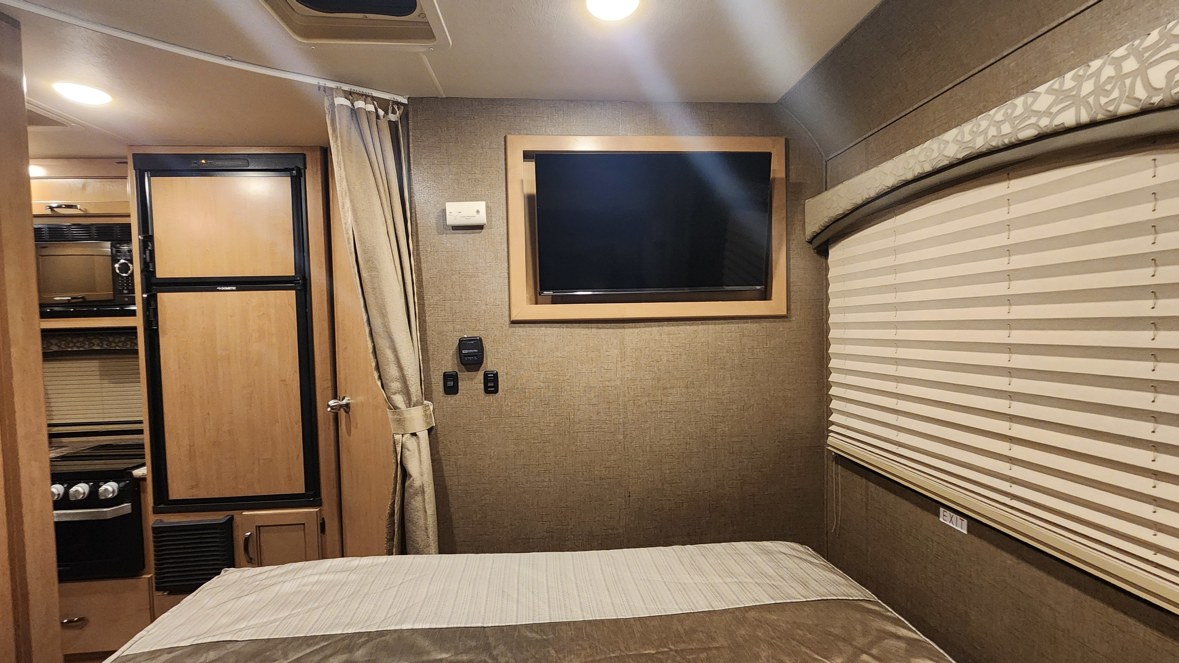 RV rental interior: A cozy bedroom with TV, complete kitchen (fridge, stove, microwave), and window with blinds.. Thor Chateau 2019