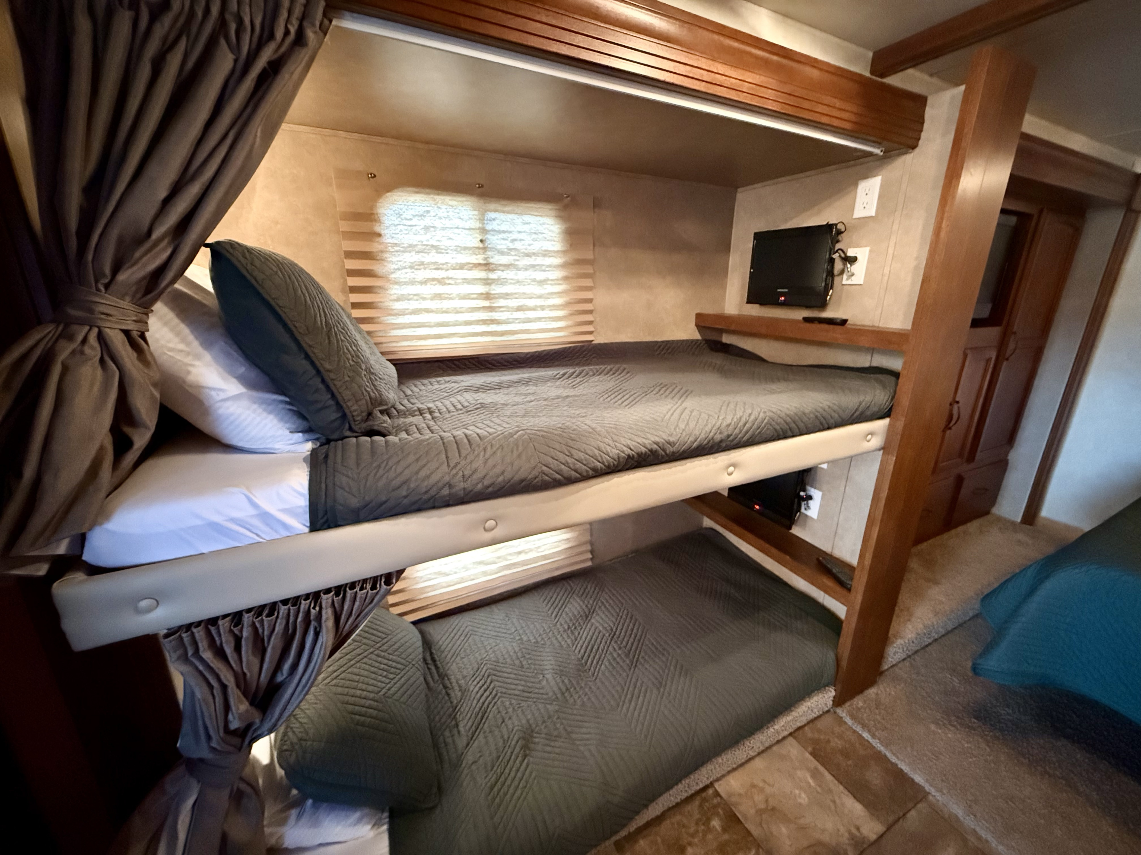 This RV rental bunk bed area features two cozy bunks with grey quilts, pillows, window blinds, and TVs, framed by wood.. Forest River Coachmen Mirada 2014