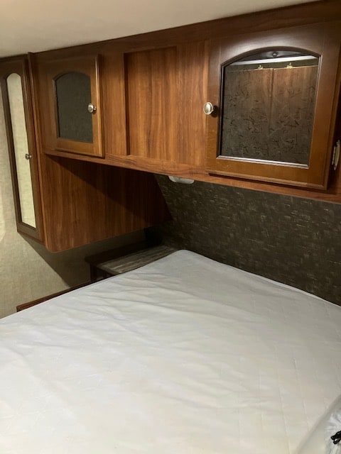 RV rental bedroom interior: white mattress, overhead wood cabinets with glass fronts, and a side mirrored closet. Cozy sleeping area.. Heartland RVs North Trail 2015