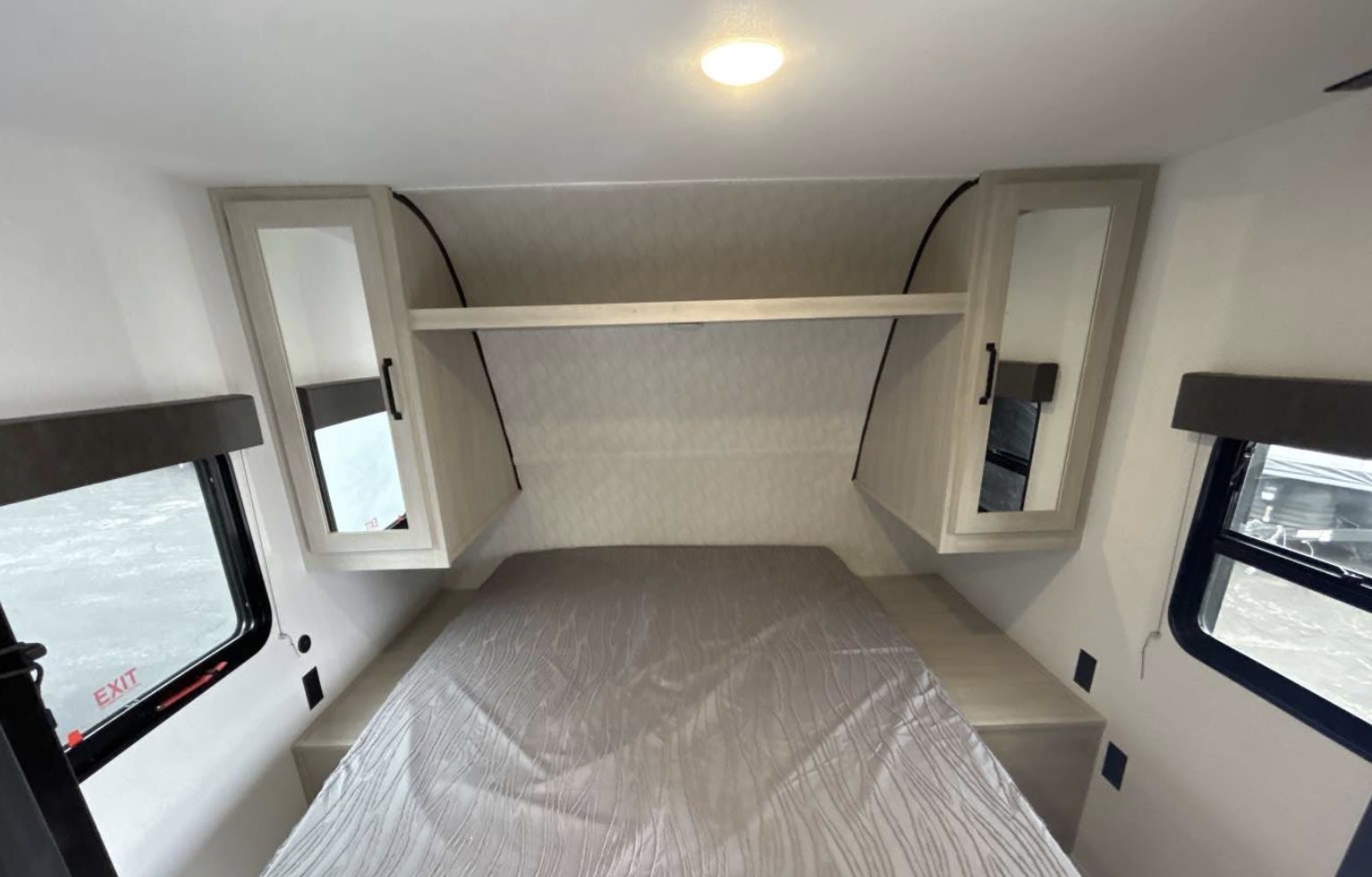 RV rental bedroom features a light bed, mirrored cabinets, storage shelf, and side windows for travel.. Forest River Palomino Puma Camping Edition 2025