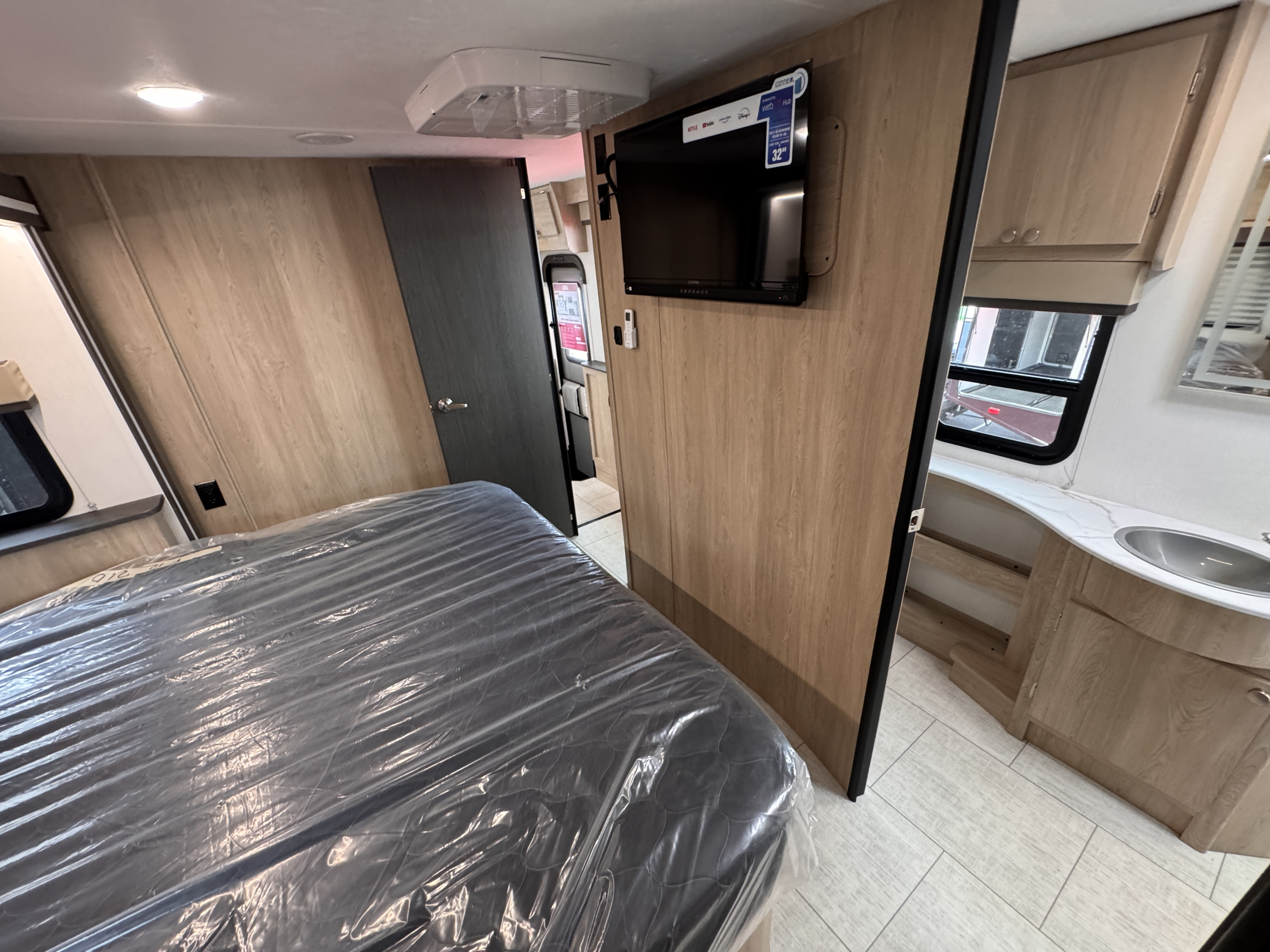 Modern RV rental interior featuring a bedroom with a plastic-covered bed, mounted TV, and a compact bathroom vanity.. Forest River Coachmen Freelander 2026