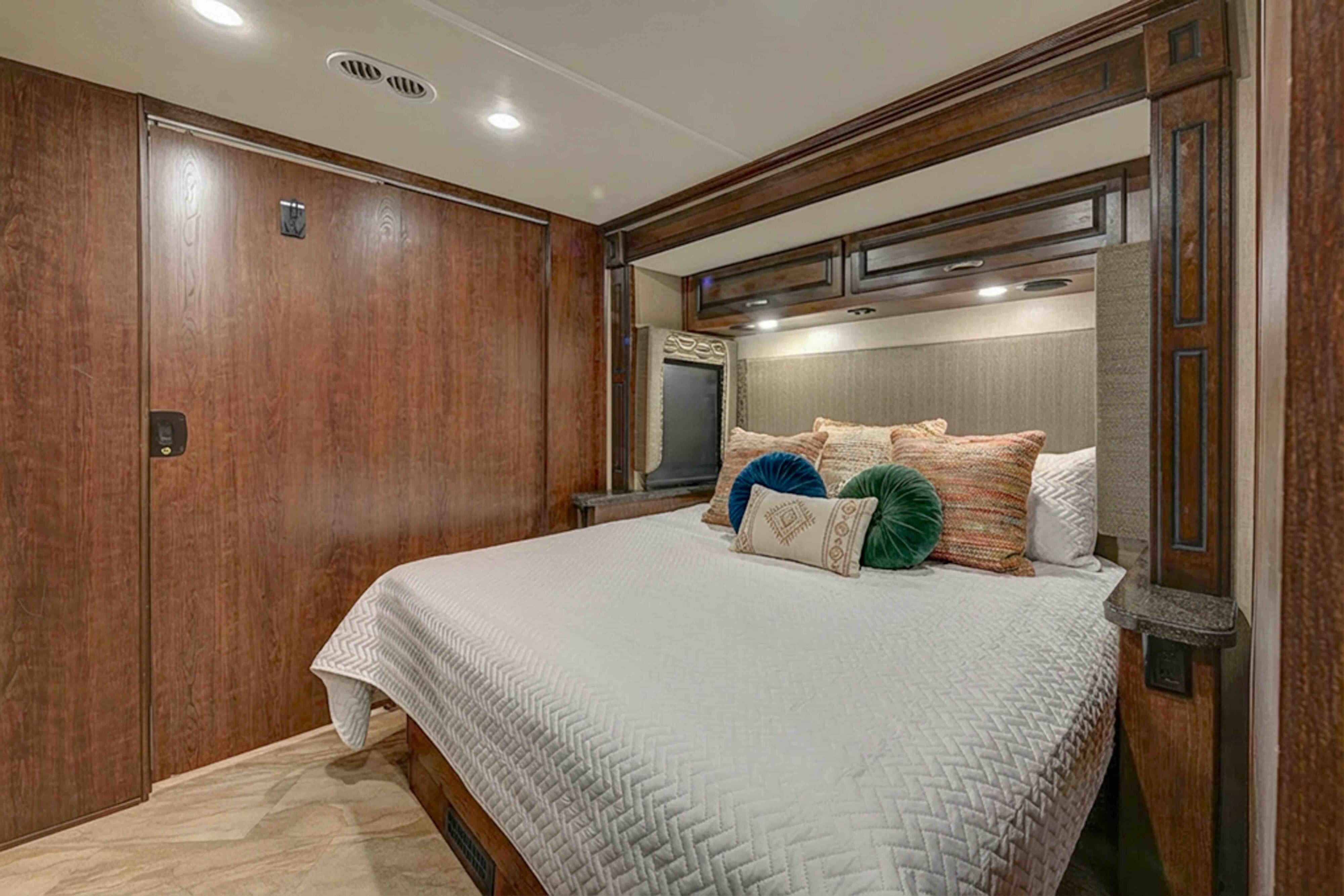 This RV rental bedroom features a cozy bed with colorful pillows, sleek wood paneling, and built-in storage for your journey.. Fleetwood Other 2017