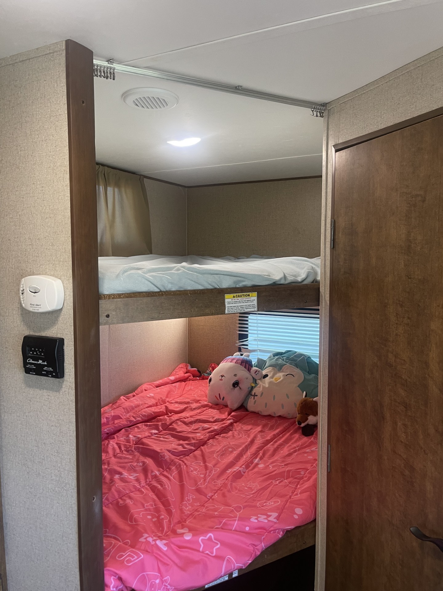RV rental's bunk beds: a lower bed with pink bedding & toys, an upper bed. Wall has a smoke detector & thermostat.. Crossroads RV Zinger 2017