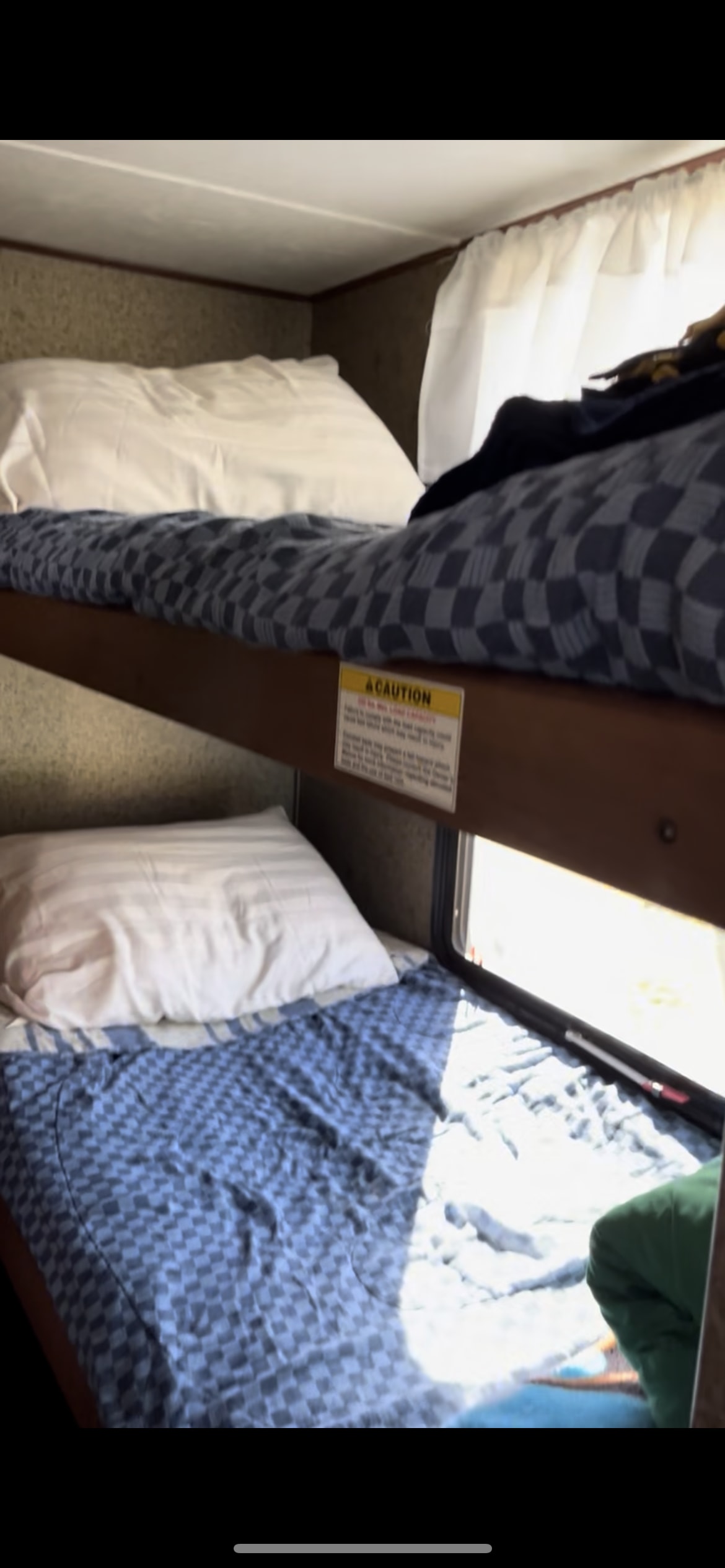 RV rental interior view: neatly made bunk beds with blue checkered bedding, white pillows, and a caution label for safety.. Crossroads RV Z-1 2013