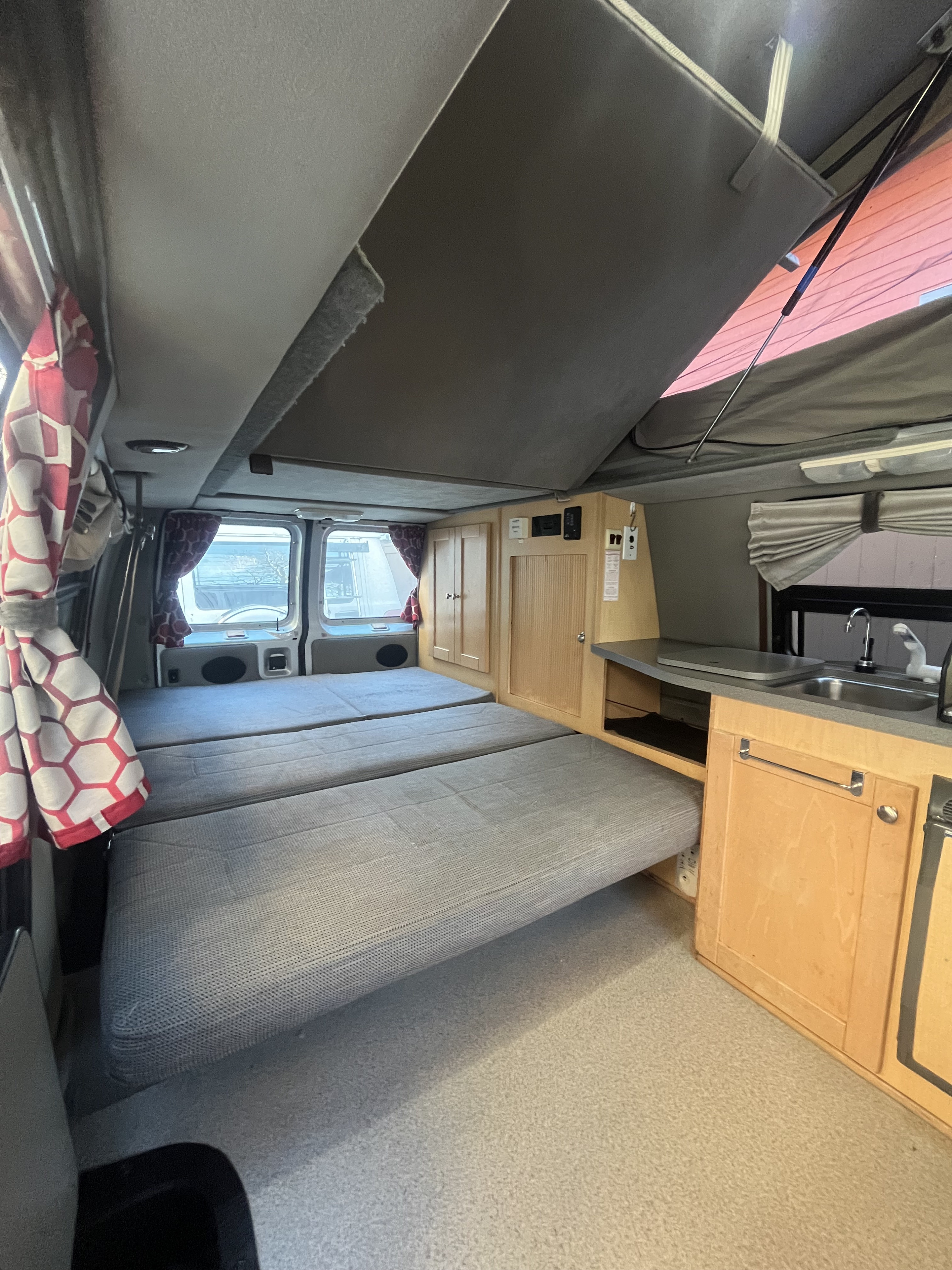 Inside an RV rental: cozy camper van interior with pop-top roof, fold-down beds, and a compact kitchenette.. Pleasure-Way Pleasure-Way Class B 2002
