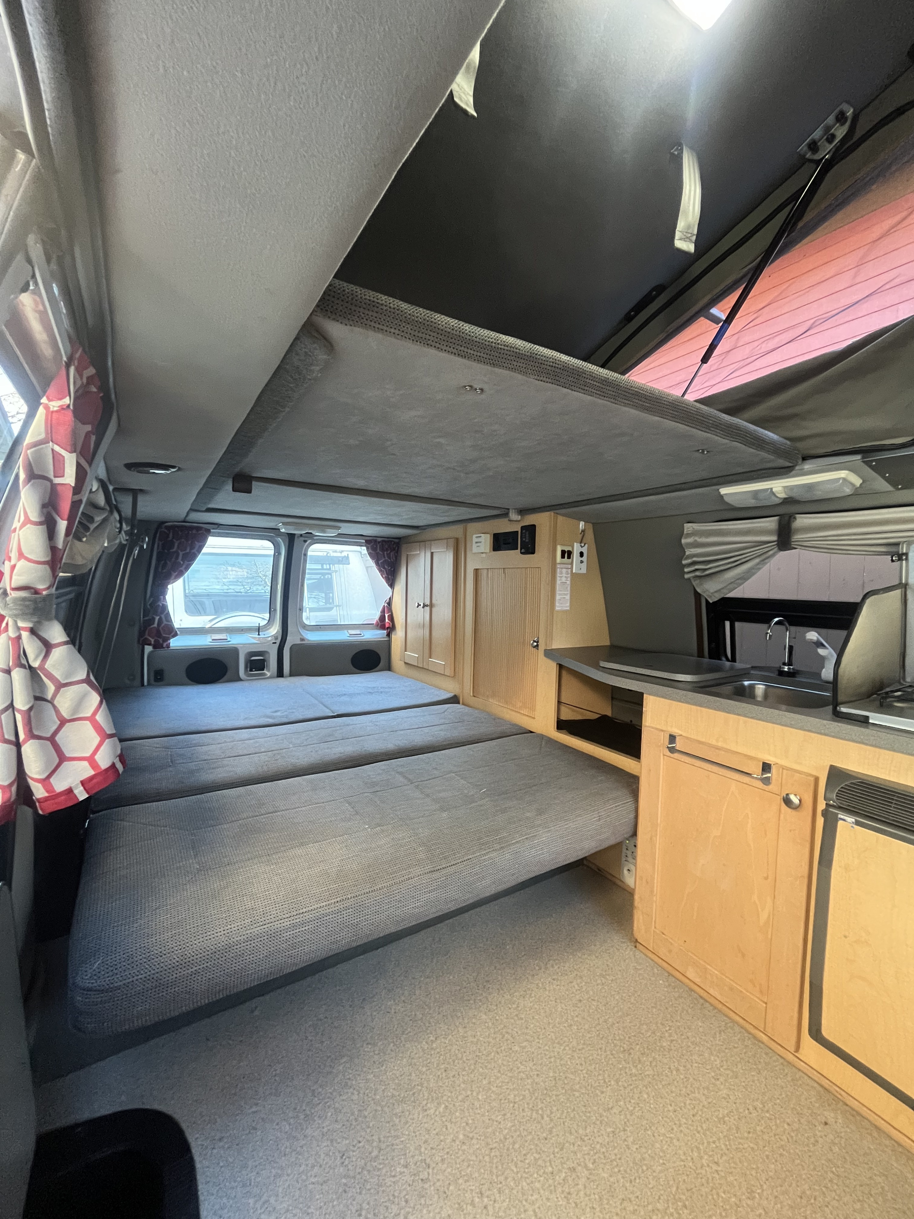 Interior of an RV rental, featuring convertible lower beds, an overhead sleeping area, and a functional kitchen with sink & stove.. Pleasure-Way Pleasure-Way Class B 2002