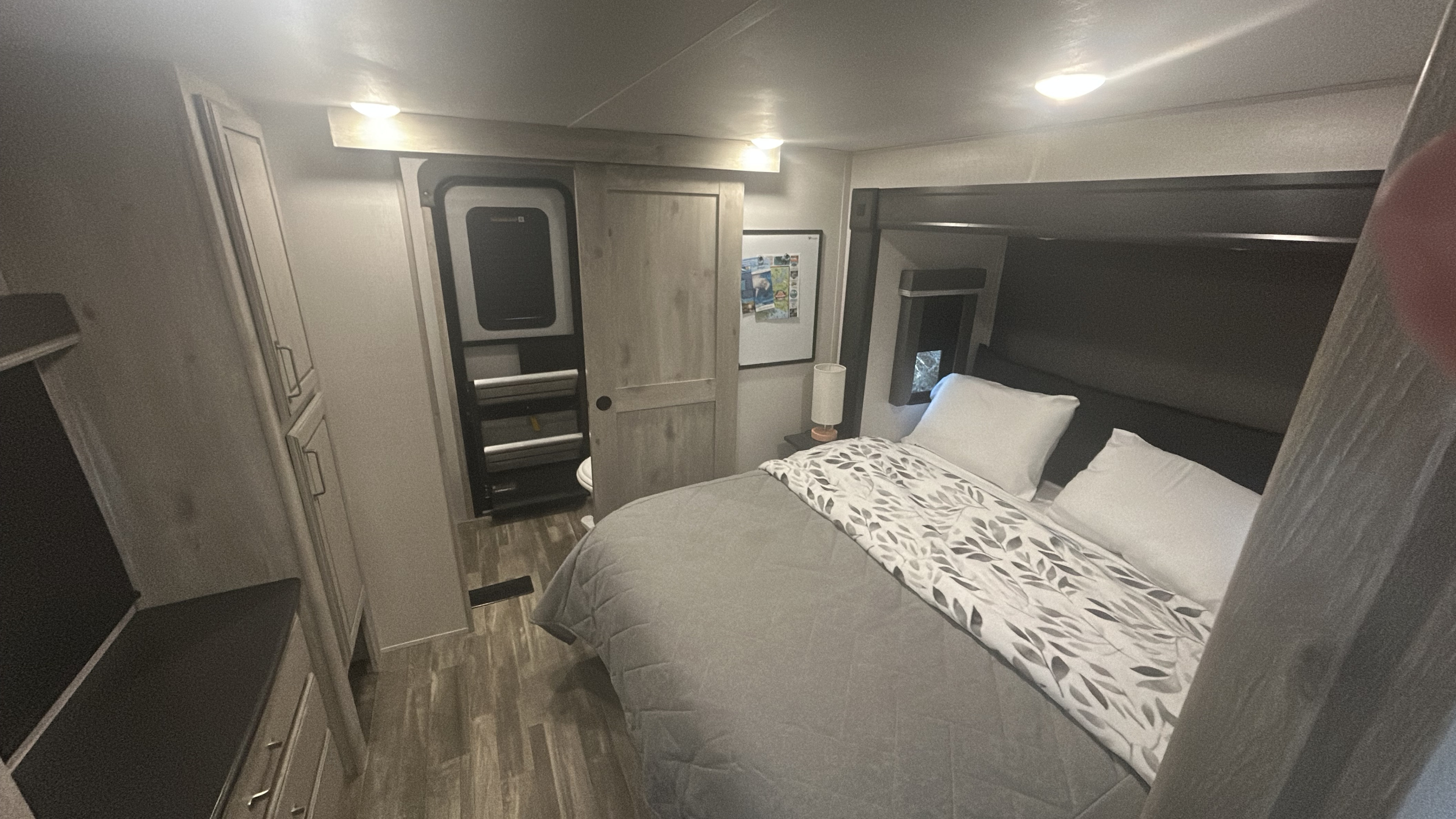 RV rental bedroom with a comfortable bed, modern decor, built-in cabinetry, and a sliding door to the bathroom.. Keystone RV Avalanche 2022
