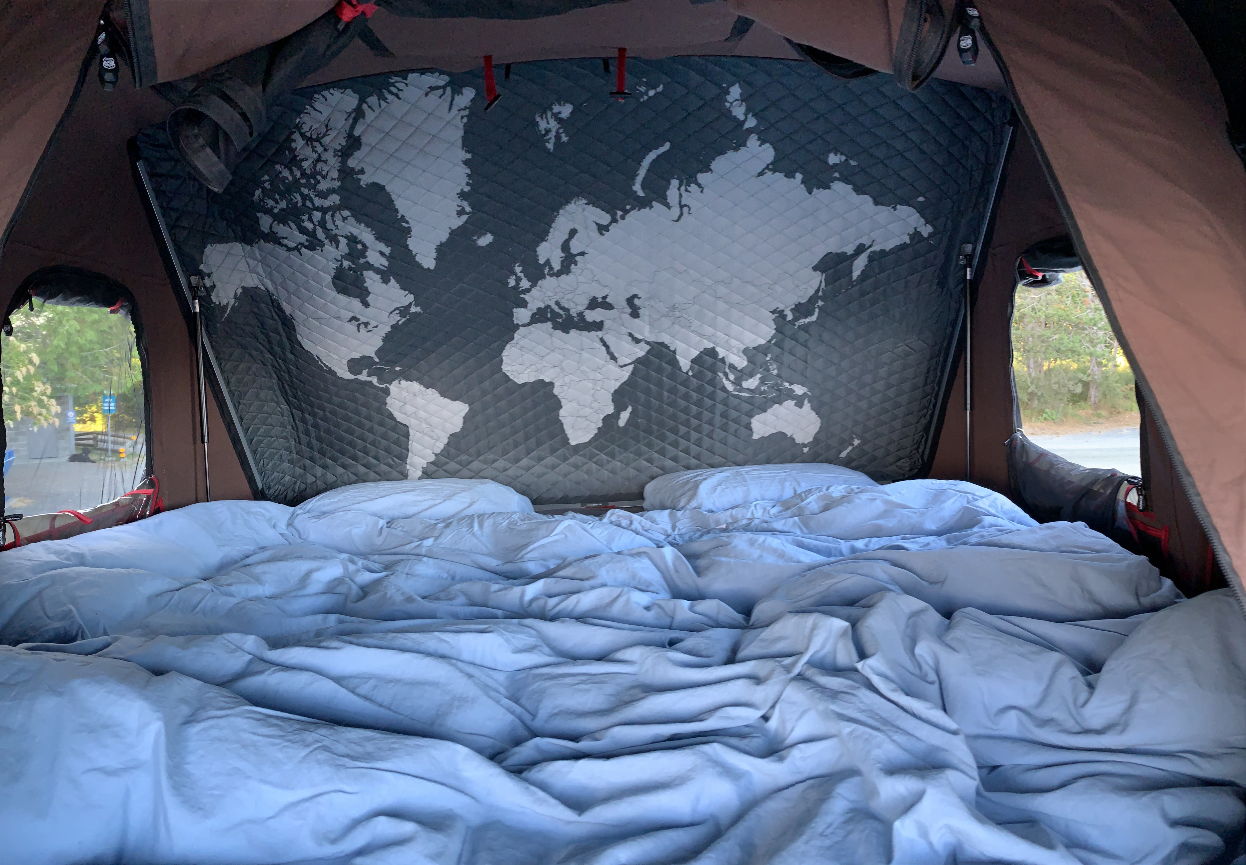Cozy RV rental rooftop tent interior. Features a comfortable bed, quilted world map decor, and windows to nature for camping.. Toyota 4Runner 2017
