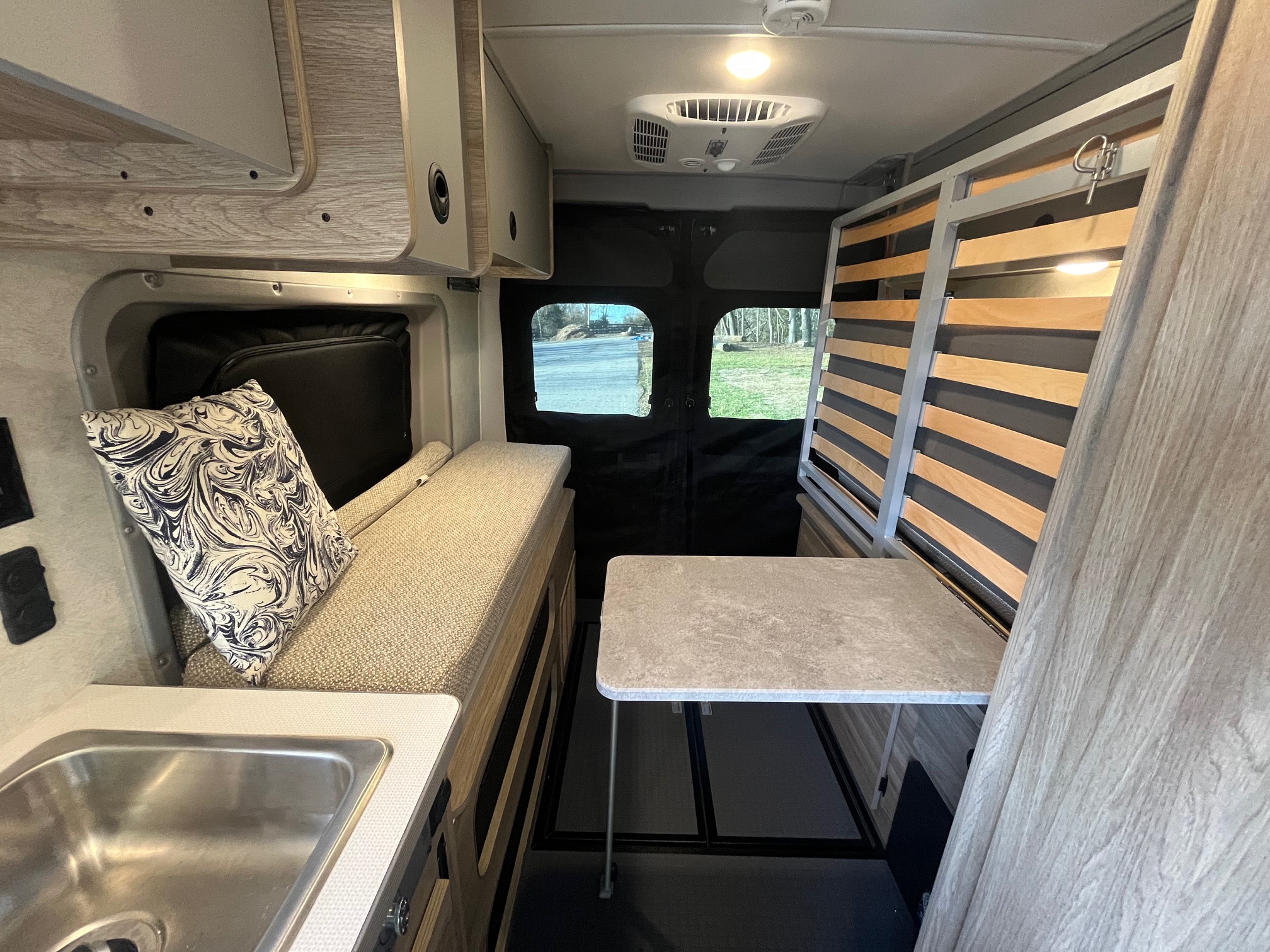 Spacious RV rental interior with kitchen sink, bench seat, table, and slatted bed frame, offering comfortable travel.. Winnebago Solis 2025