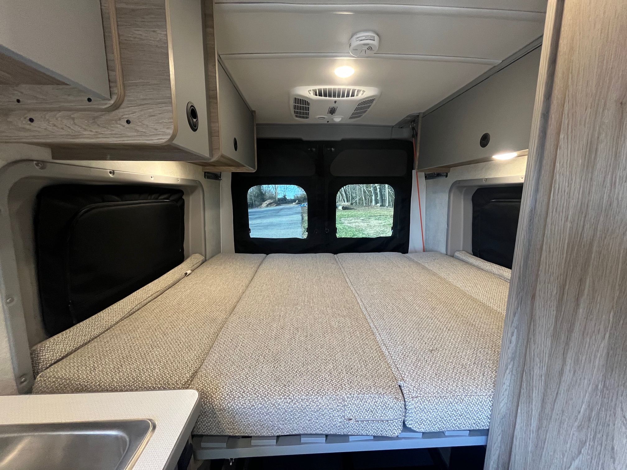 Comfortable RV rental interior with a bed, overhead cabinets, AC unit, and rear windows showcasing outdoor scenery.. Winnebago Solis 2025