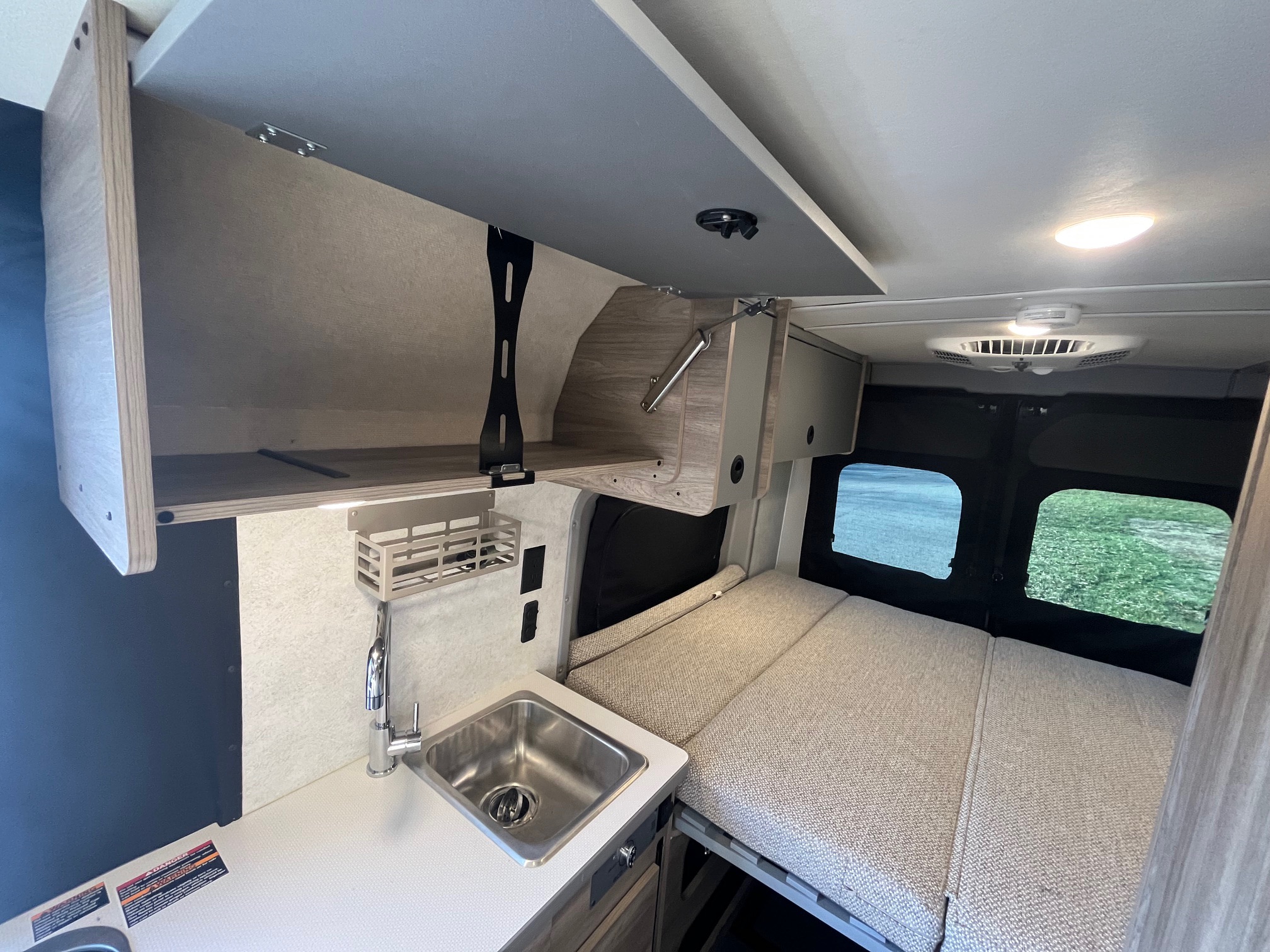 RV rental interior: cozy campervan kitchenette with sink, open overhead storage, and comfortable bed for your next adventure.. Winnebago Solis 2025