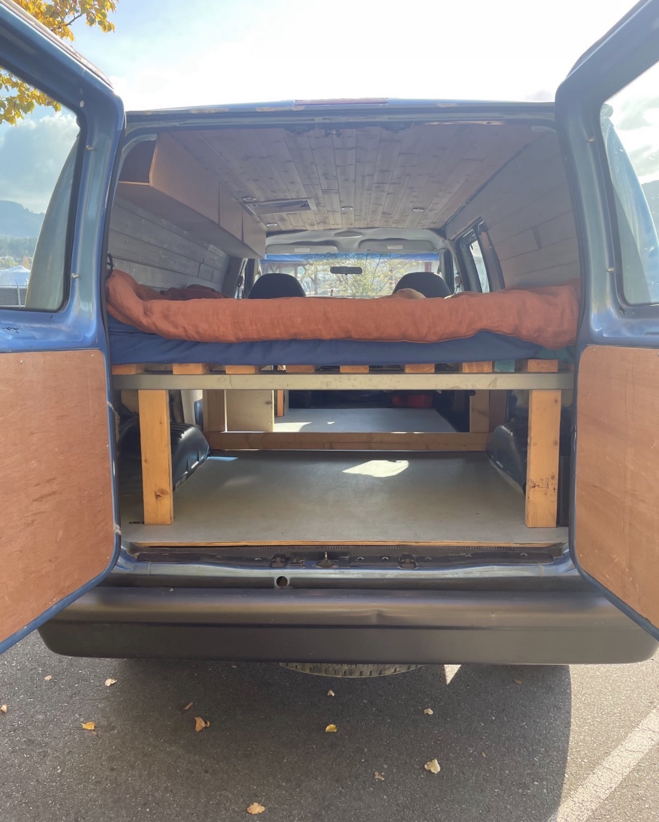RV rental: Blue converted van's rear view. Doors open to a raised bed, wood-paneled interior, ready for adventure.. Ford Econolline 250s 2006