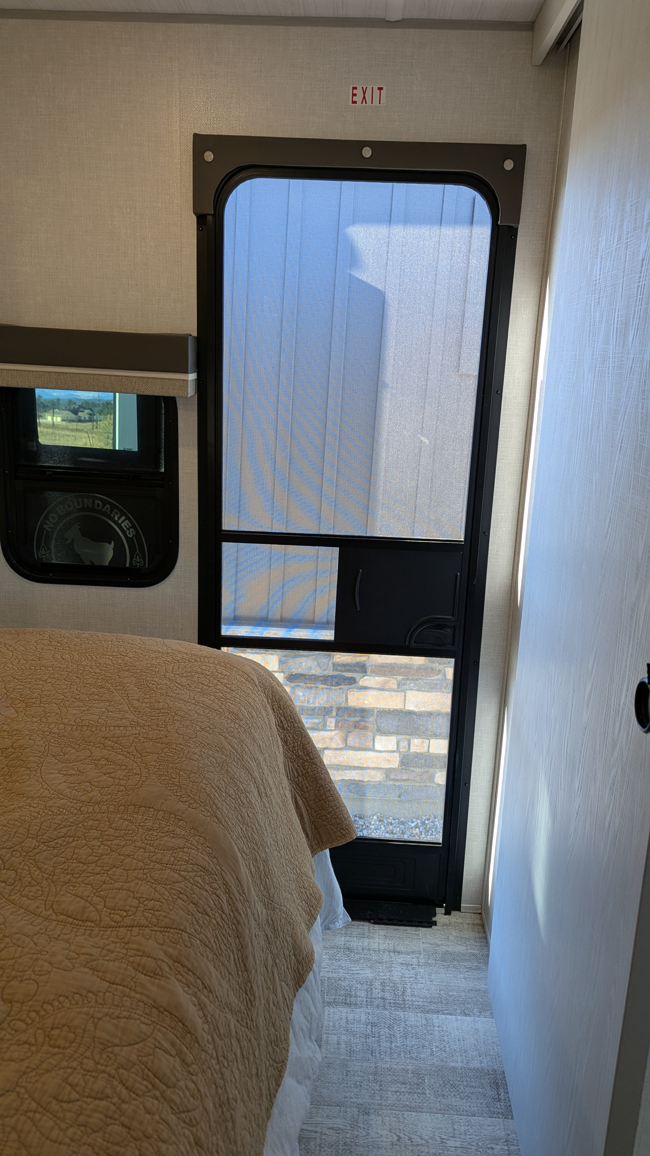 Cozy RV rental bedroom featuring a bed, window, and an essential exit screen door, marked by an "EXIT" sign overhead.. No Boundaries 20 2025