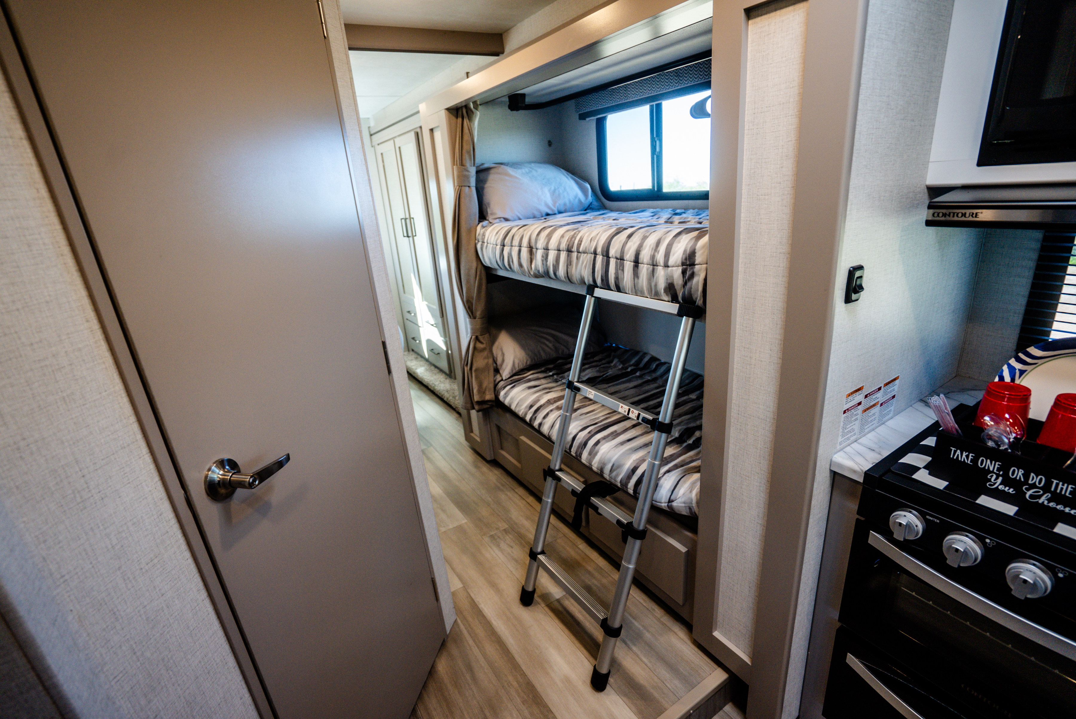 Cozy rv rental interior featuring bunk beds with a ladder, a window, and a compact kitchen area with a stove.. Thor Geneva 2026