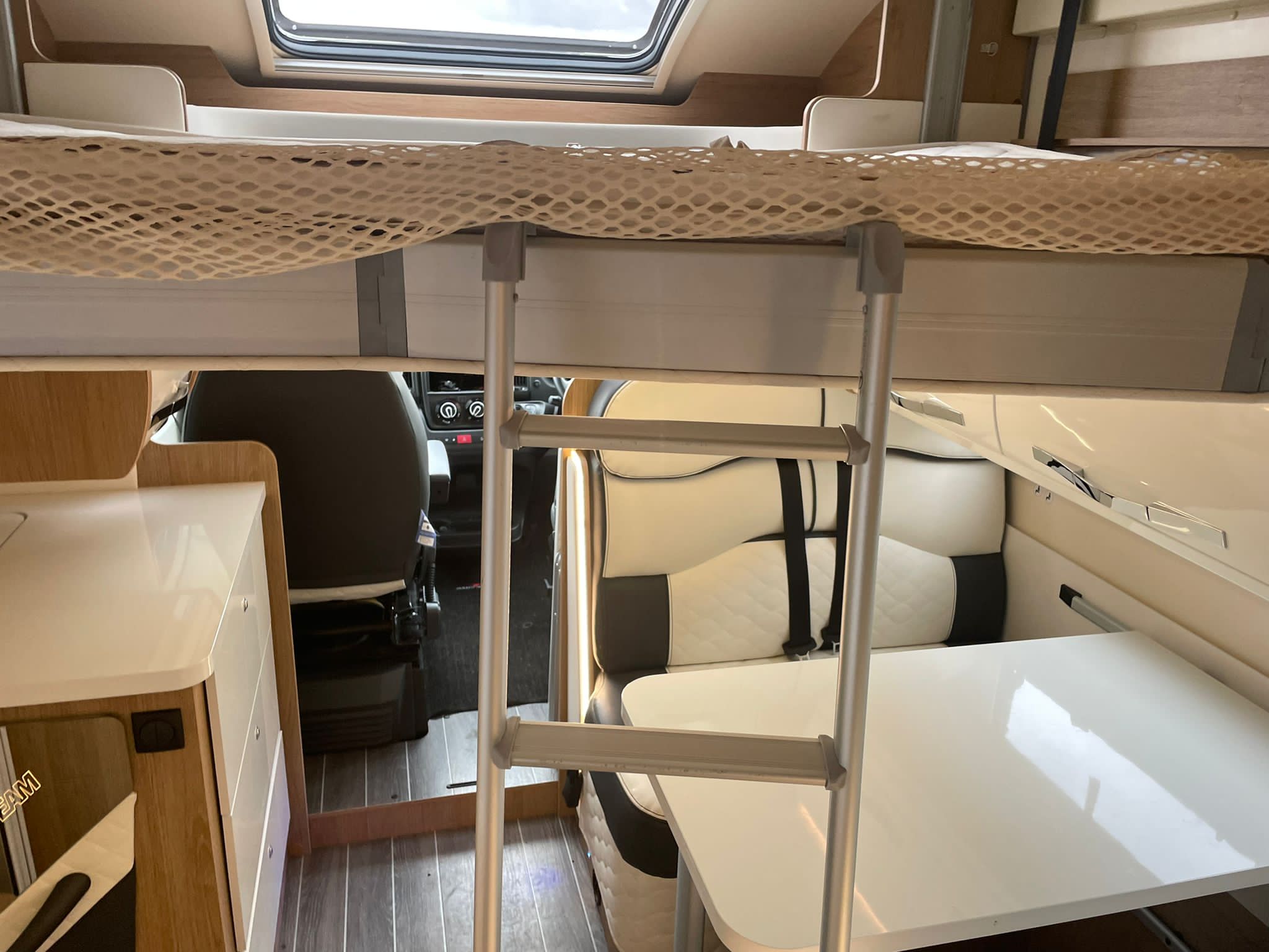 RV rental interior featuring a bunk bed with safety net & ladder, dining area, and compact kitchen.. Rollerteam Autoroller 747 2021