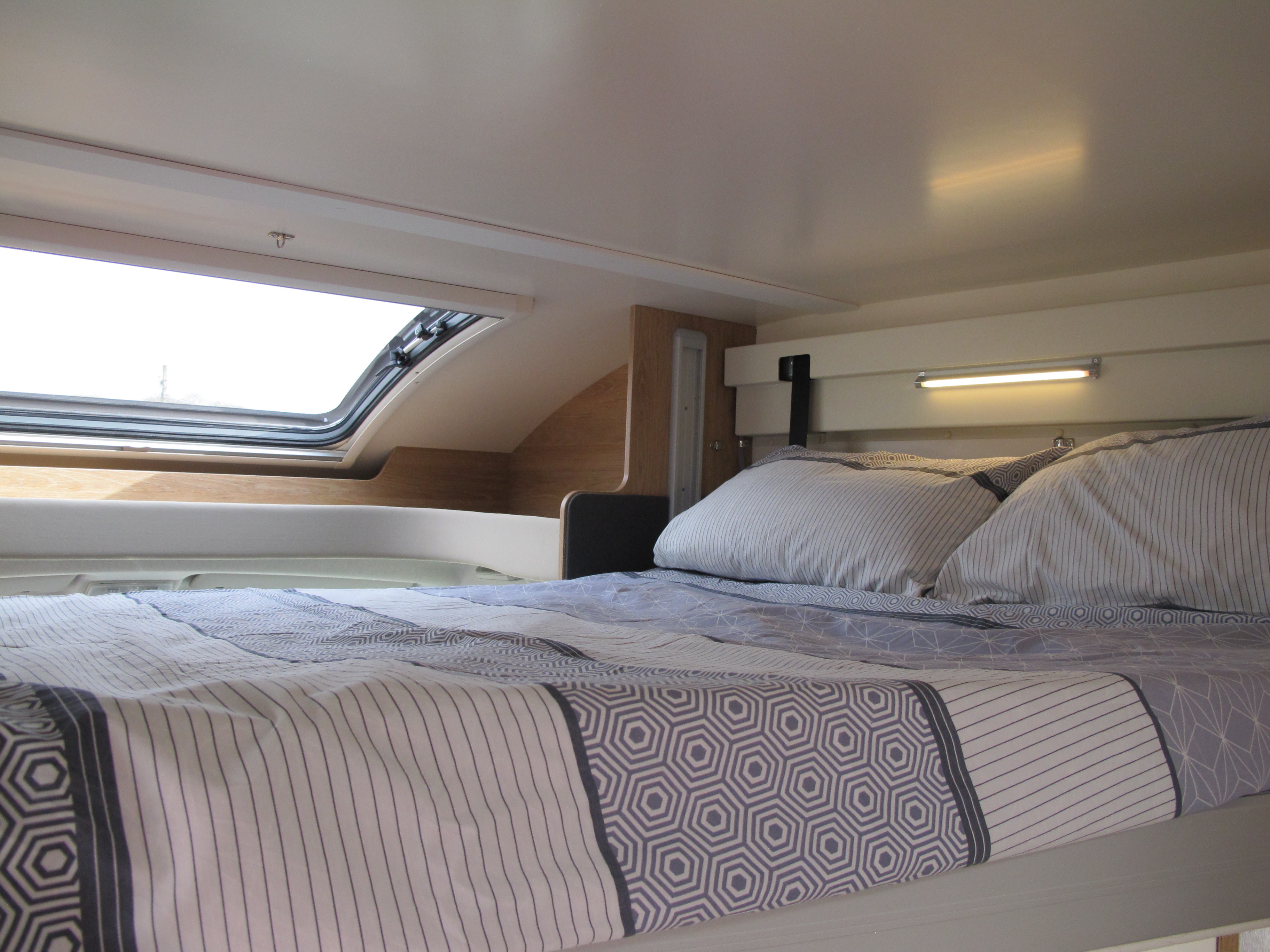 Cozy RV rental bedroom with patterned bed, pillows, and a large roof window. Perfect sleeping area for travel.. rollerteam 747 2021