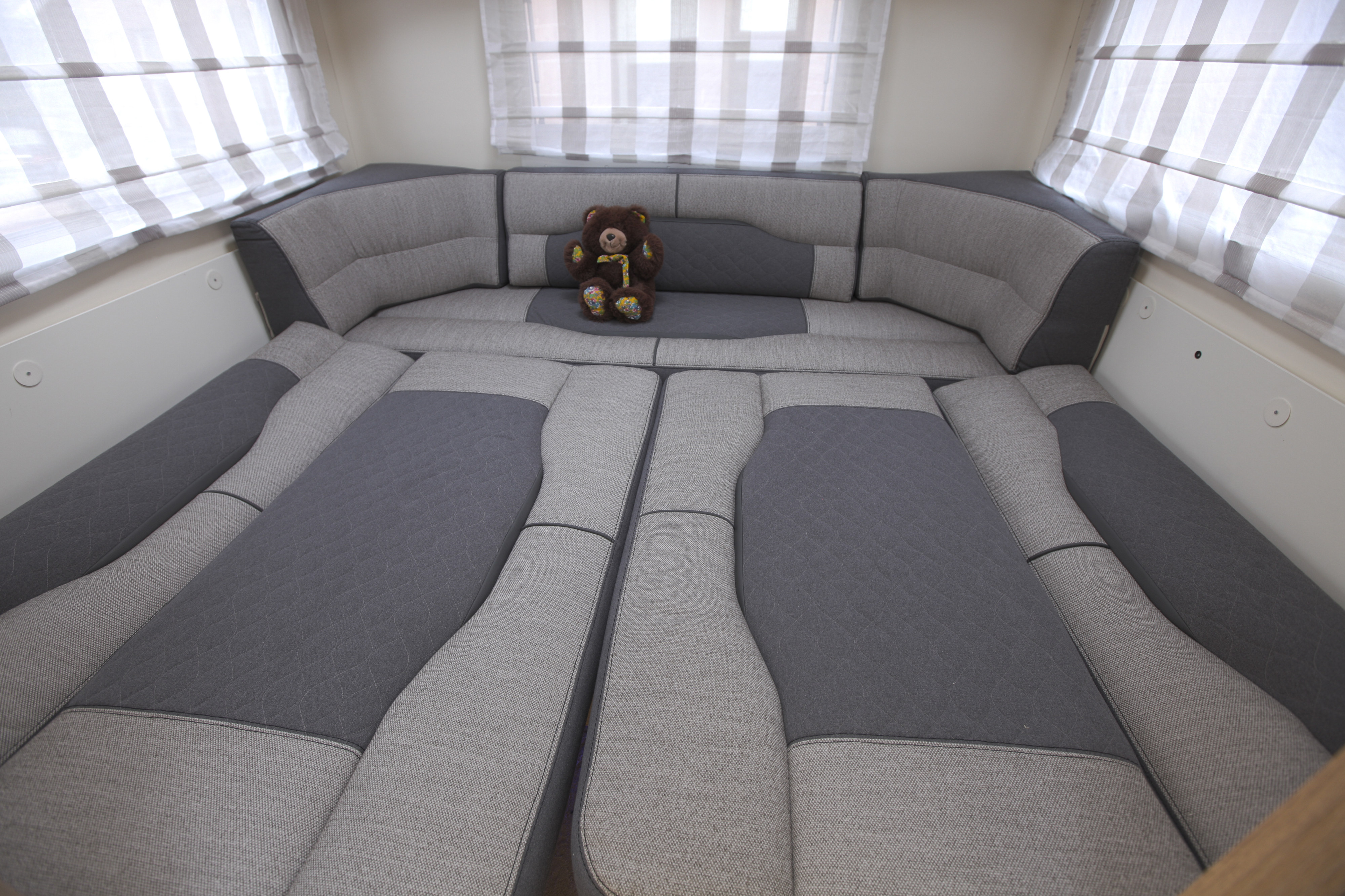 Cozy rv rental interior: Rear seating converted to a bed with two-tone grey cushions & a teddy bear. Striped window blinds.. rollerteam 747 2021