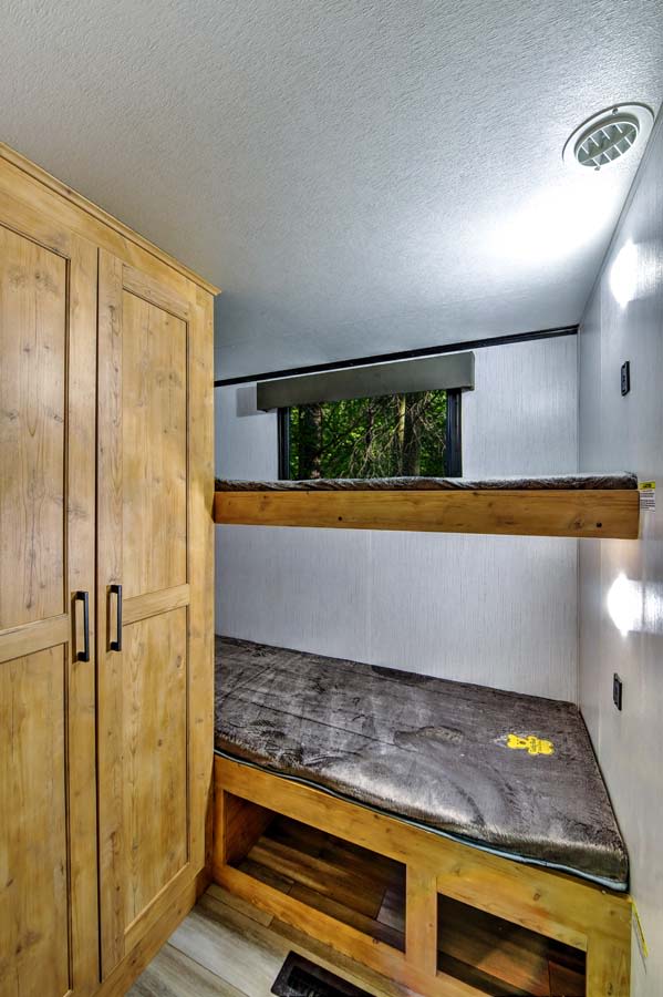 RV rental interior: Wooden bunk beds, closet, and window with outdoor view. Cozy sleeping area with under-bed storage.. Heartland RVs Milestone 2023