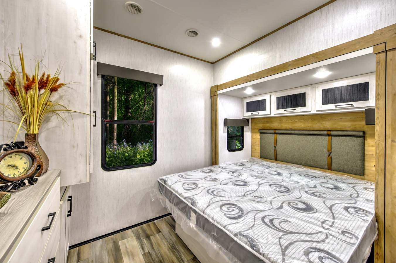 Modern RV rental bedroom interior with a comfortable bed, overhead storage, and nature views from windows.. Heartland RVs Milestone 2023