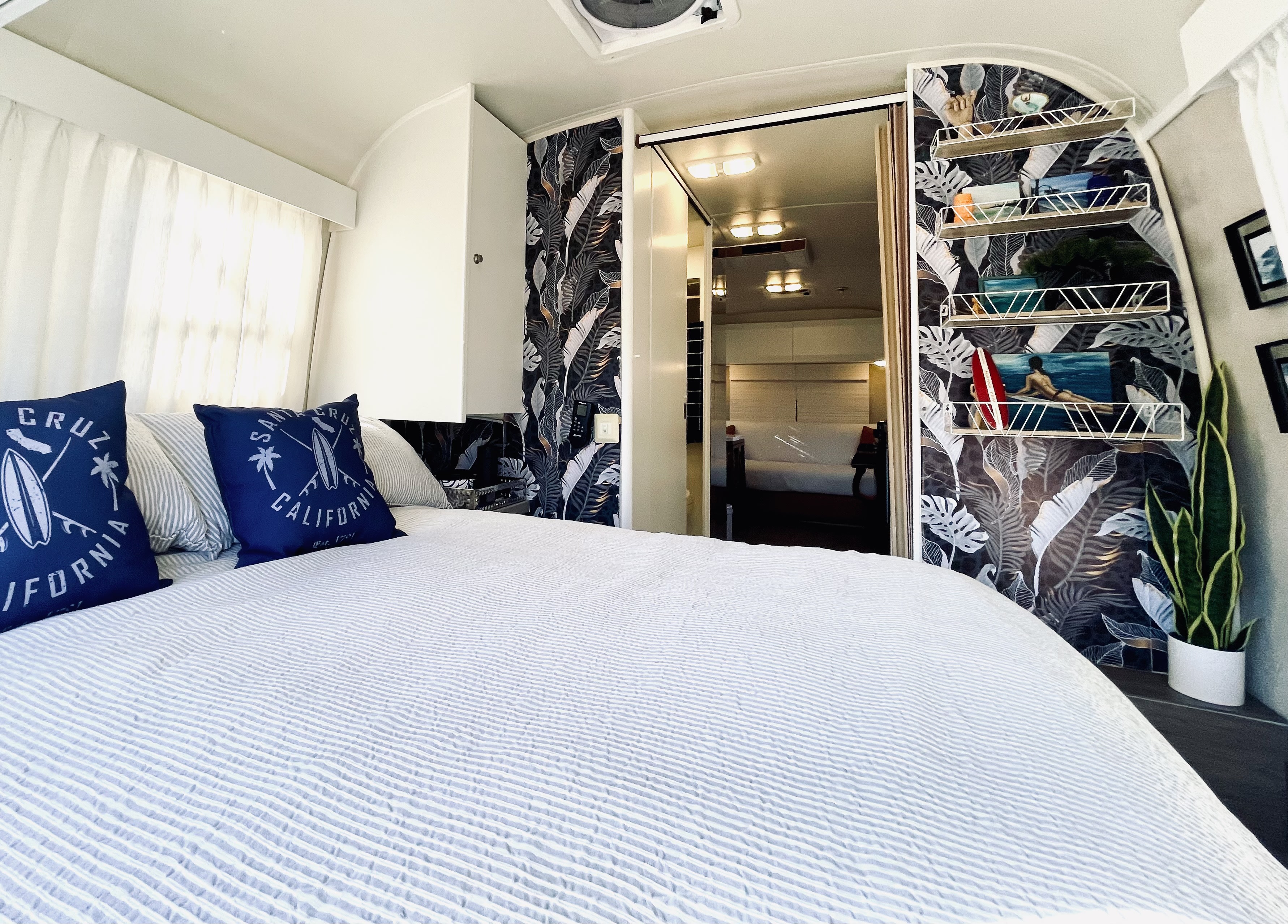 Cozy rv rental interior: bed with striped bedding, tropical wallpaper, and shelves. View into the main living area.. Airstream Safari 2002