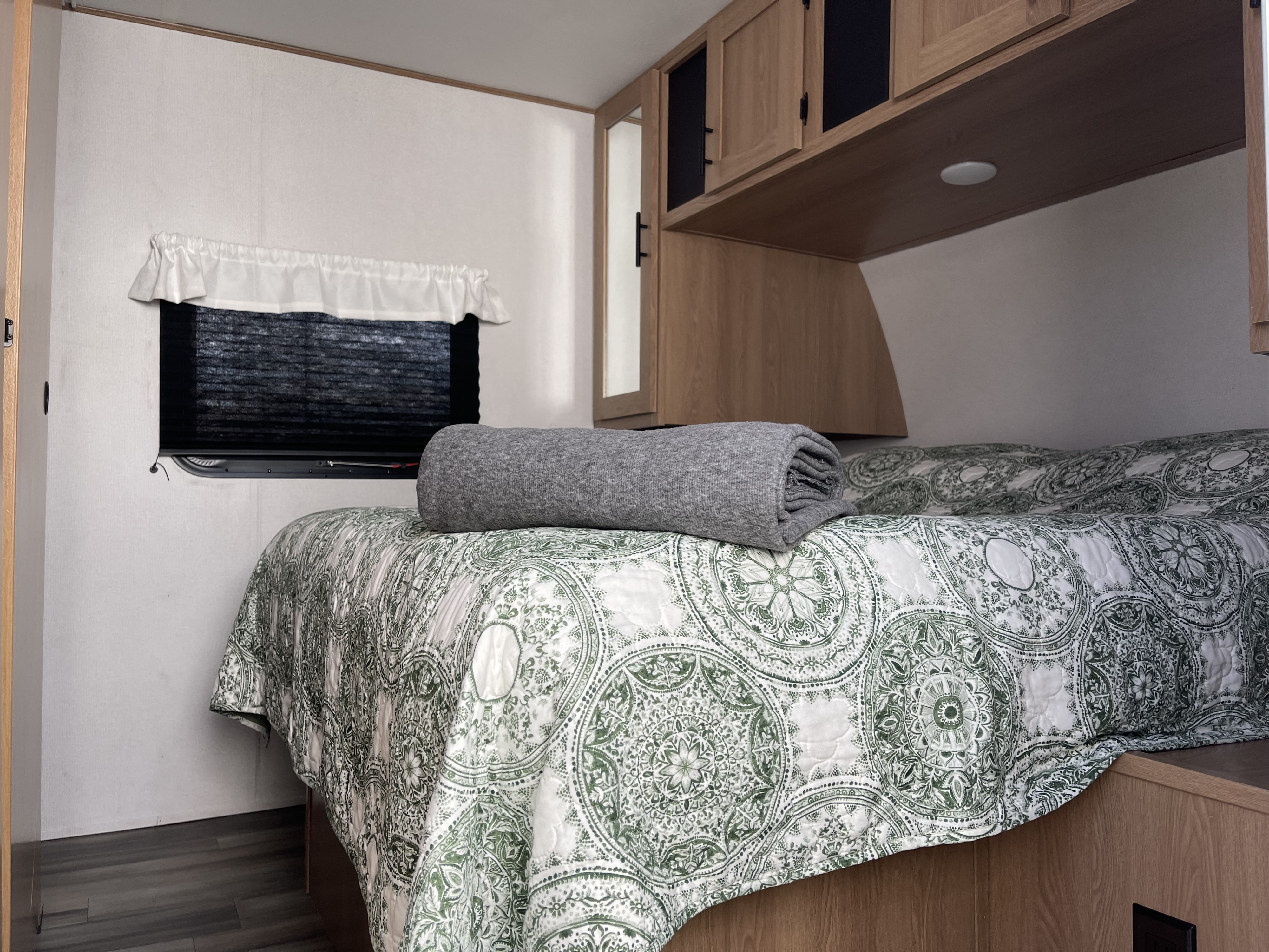 Cozy rv rental bedroom with a green patterned quilt, gray blanket, and wooden overhead storage, ready for your next adventure.. Avenger Avenger Trailer 2022