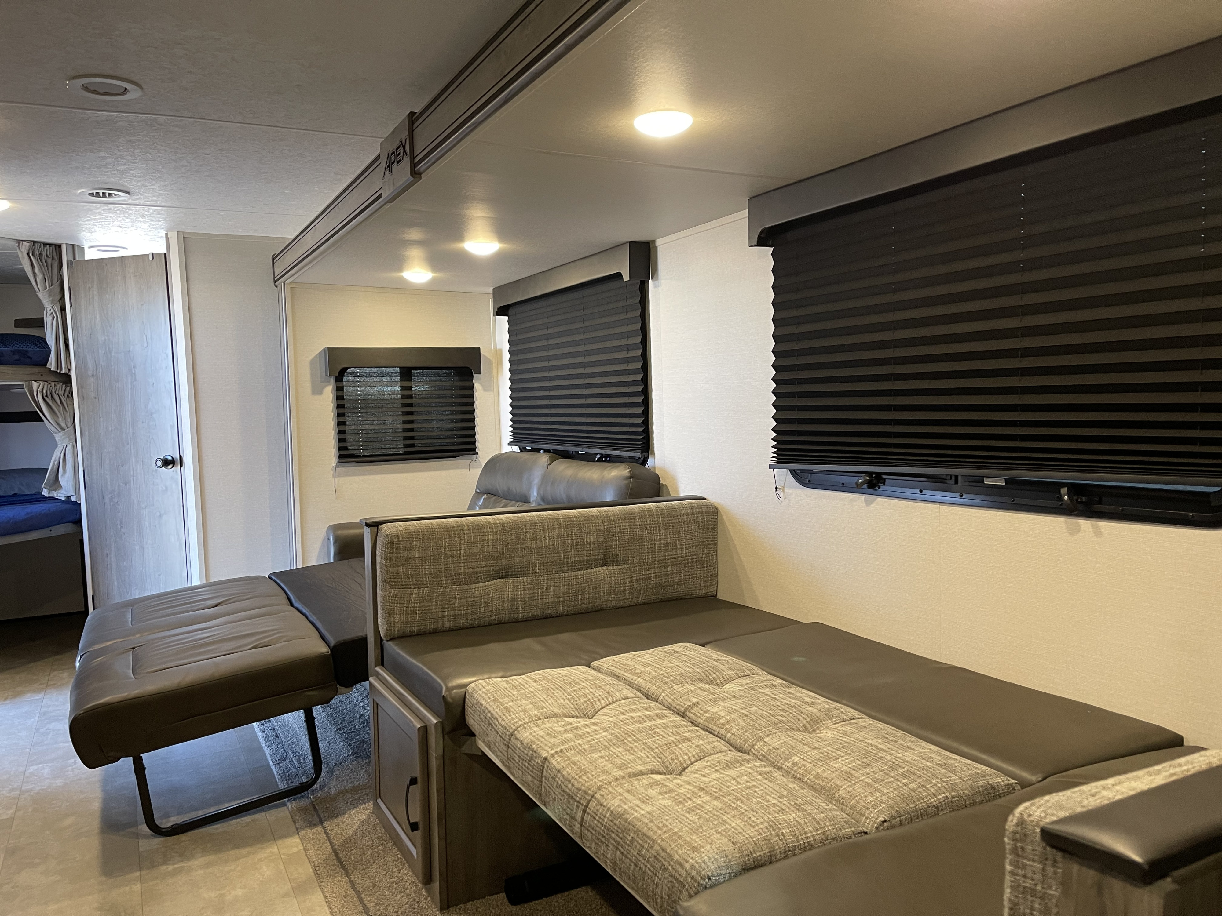 RV rental interior: A versatile lounge/dinette converts to a bed, featuring bunk beds, black blinds, and bright overhead lights.. Coachmen Apex 2021