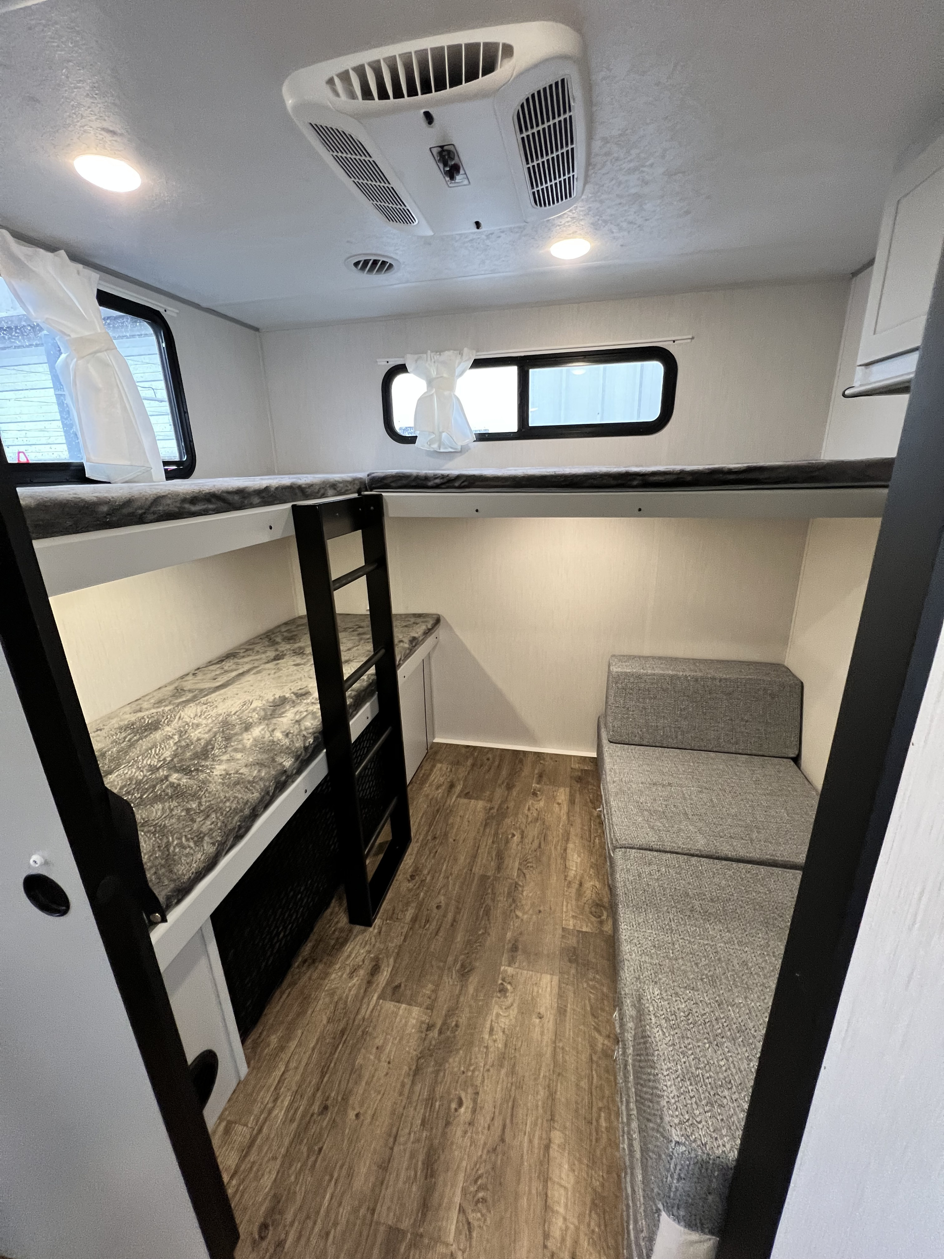 RV rental interior featuring stacked bunk beds with a ladder, a grey sofa, wood-look flooring, and ceiling AC.. Forest River Vibe 2021