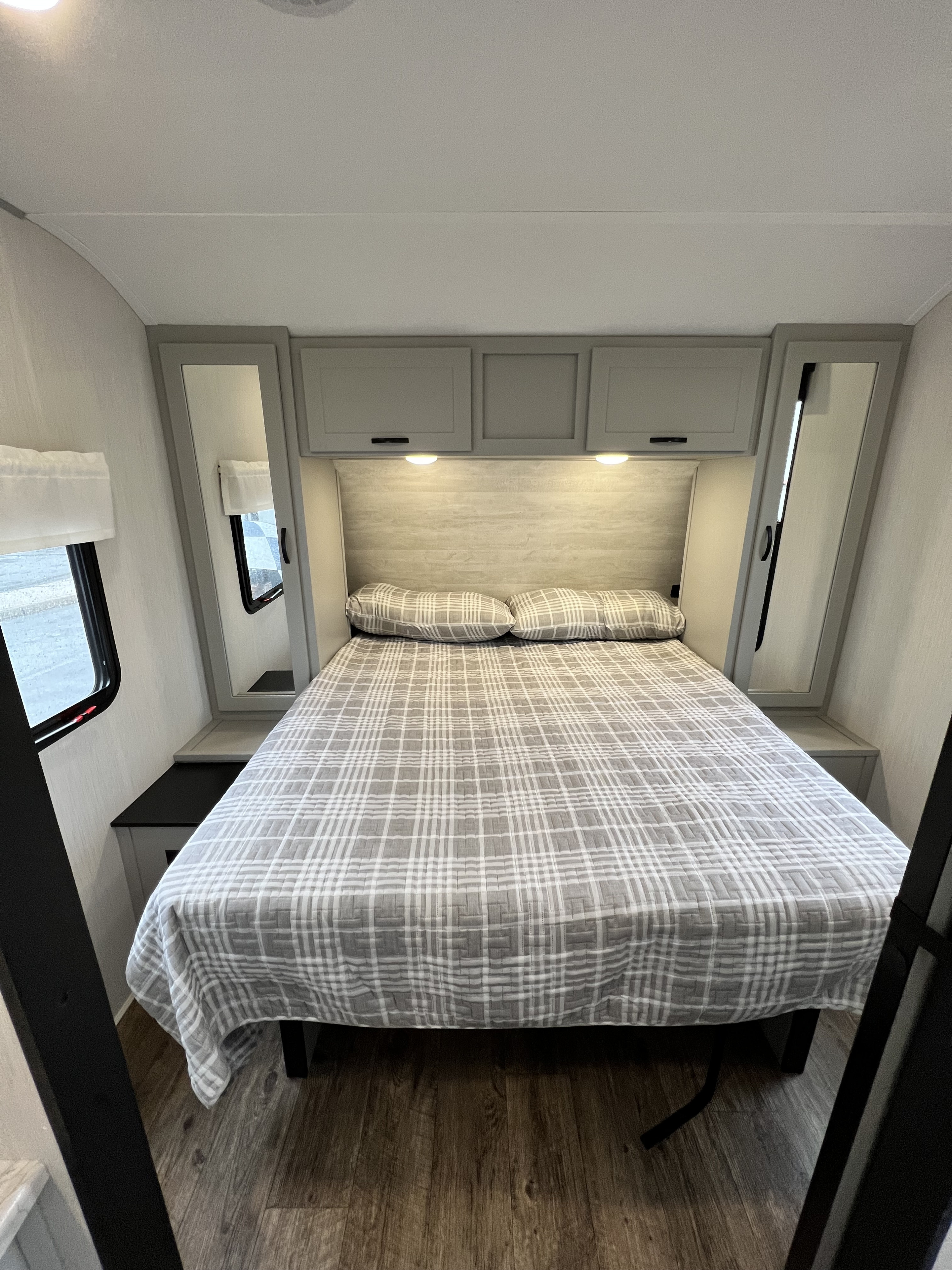 Cozy RV rental bedroom featuring a queen bed with gray plaid bedding, overhead storage, and mirrored wardrobes. Ideal for travel comfort.. Forest River Vibe 2021