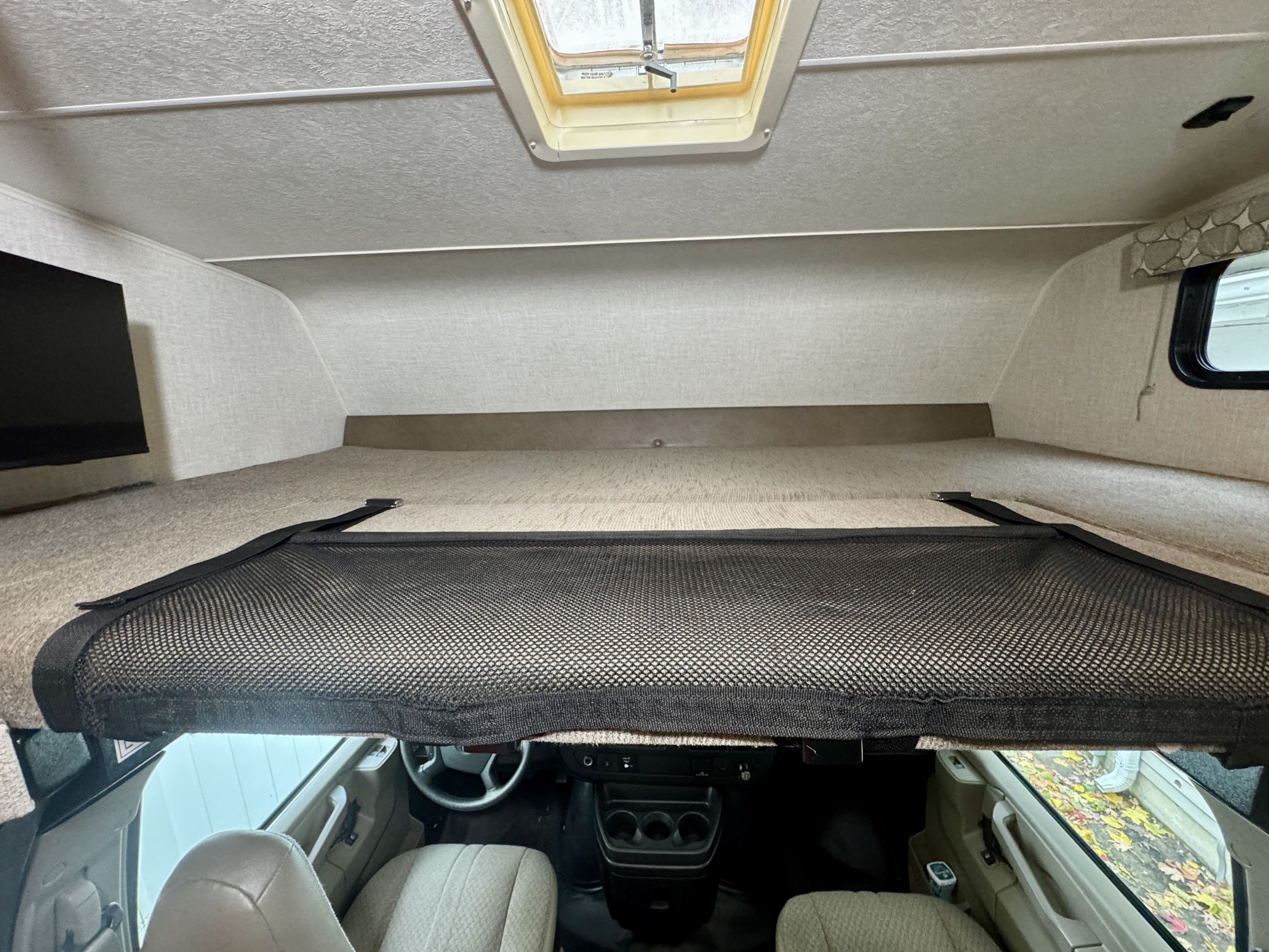 Overhead bunk bed with safety net in an RV rental, looking into the driver's cab, with a skylight overhead.. Coachman Freelander 27QB 2019