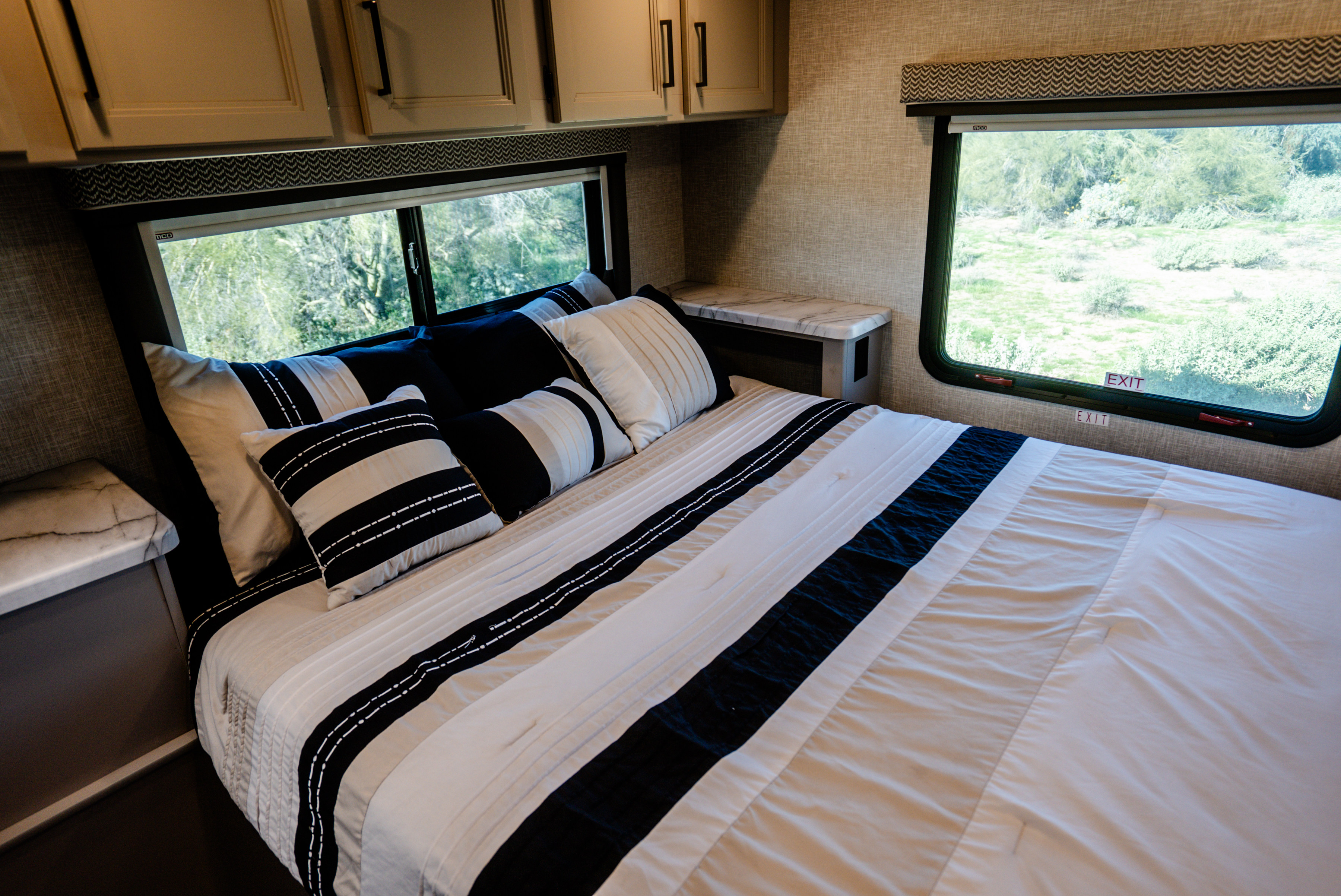 Cozy RV rental bedroom interior with a comfortable bed, stylish bedding, and large windows overlooking nature. Ideal for travel.. Thor Geneva 2026